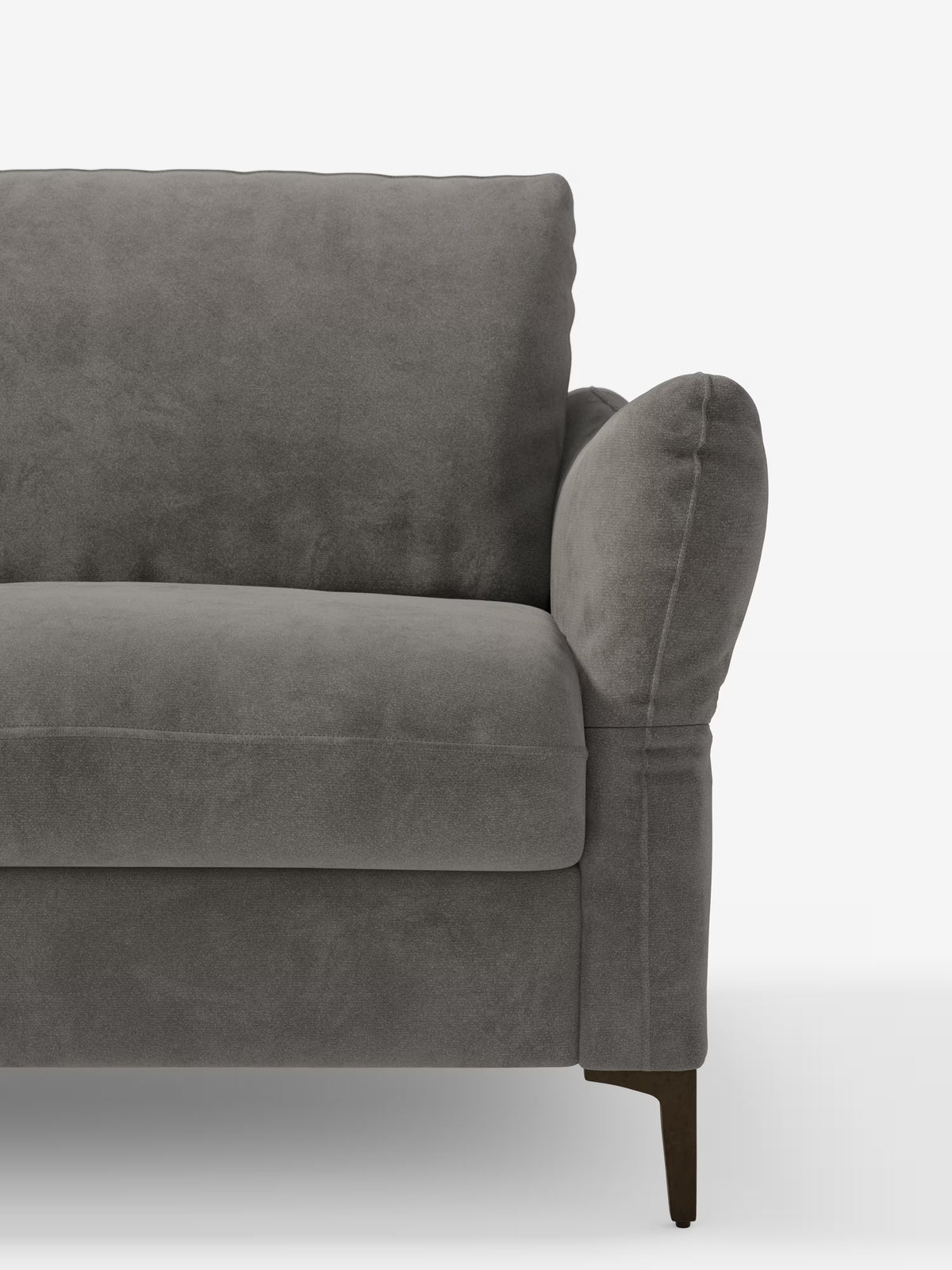 Viene mostrato un primo piano della metà sinistra del divano letto Dalia di Divani.Store su uno sfondo bianco a tinta unita, con morbidi cuscini, un bracciolo arrotondato e gambe in legno scuro. Il divano è rivestito in un moderno tessuto di velluto T30 grigio, resistente alle macchie.