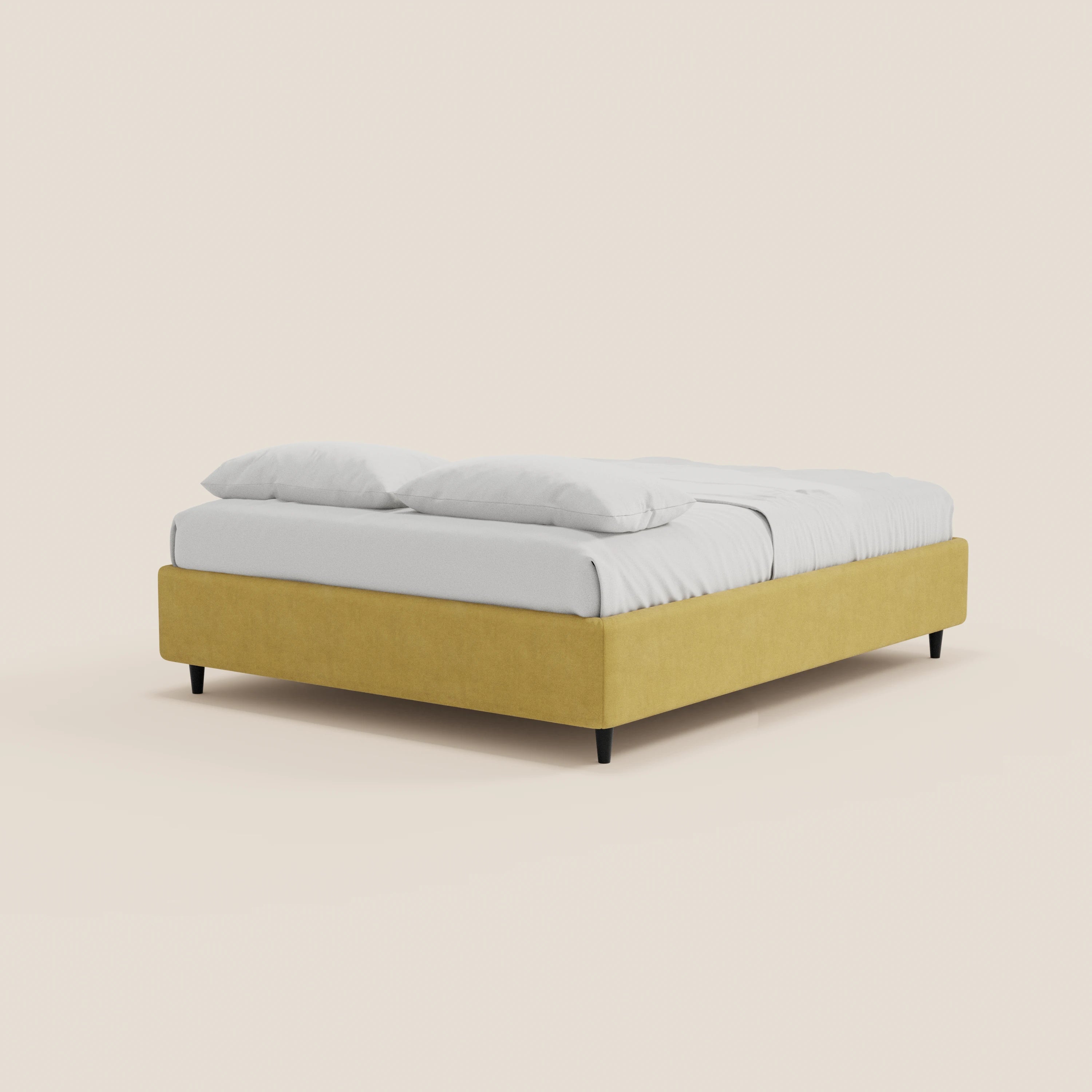Il letto sommier imbottito con contenitore ERON di Letti.store è rivestito in tessuto impermeabile giallo senape certificato Oeko-Tex, è dotato di biancheria da letto bianca e due cuscini bianchi, ha gambe nere ed è presentato su uno sfondo beige chiaro per un look elegante.