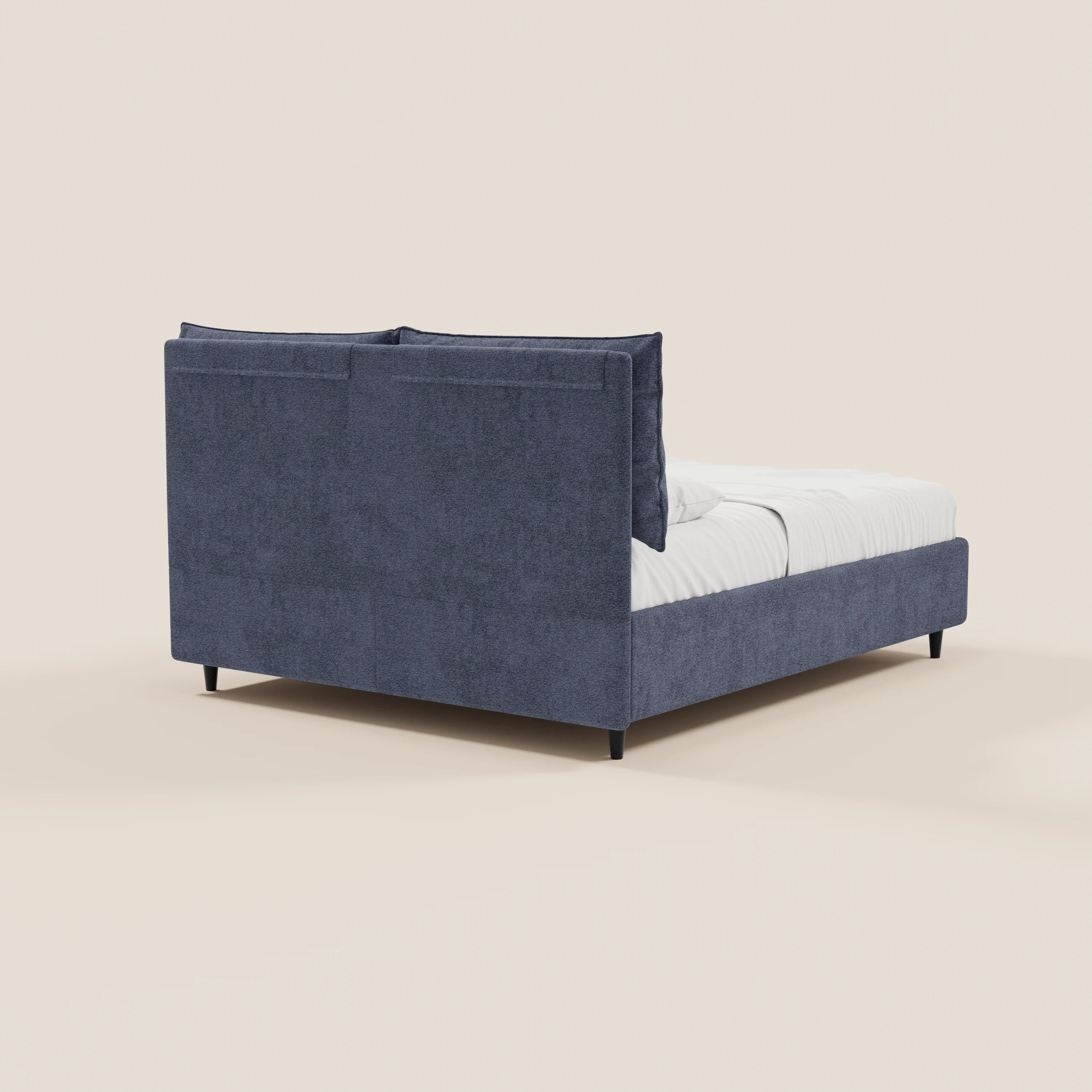 Il letto imbottito ZAYRON di Letti.store presenta un vano contenitore, una testiera con morbidi cuscini regolabili in tessuto Oeko-Tex®, una struttura blu scuro, biancheria da letto bianca e gambe nere, visto da dietro su uno sfondo beige chiaro.