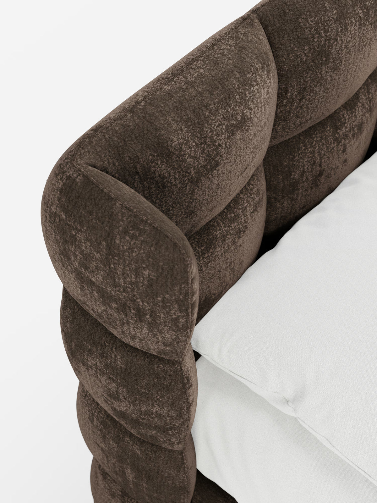 Primo piano della testiera imbottita in morbido tessuto marrone scuro del modello RAGNAR di Letti.store, un letto imbottito con contenitore e testiera capitonné avvolgente, caratterizzata da un design testurizzato e trapuntato che richiama la classica lavorazione capitonné. Accanto ad essa sono appoggiati due morbidi cuscini bianchi, il tutto su uno sfondo bianco brillante. L’elegante testiera è realizzata in tessuto certificato Oeko-Tex®.