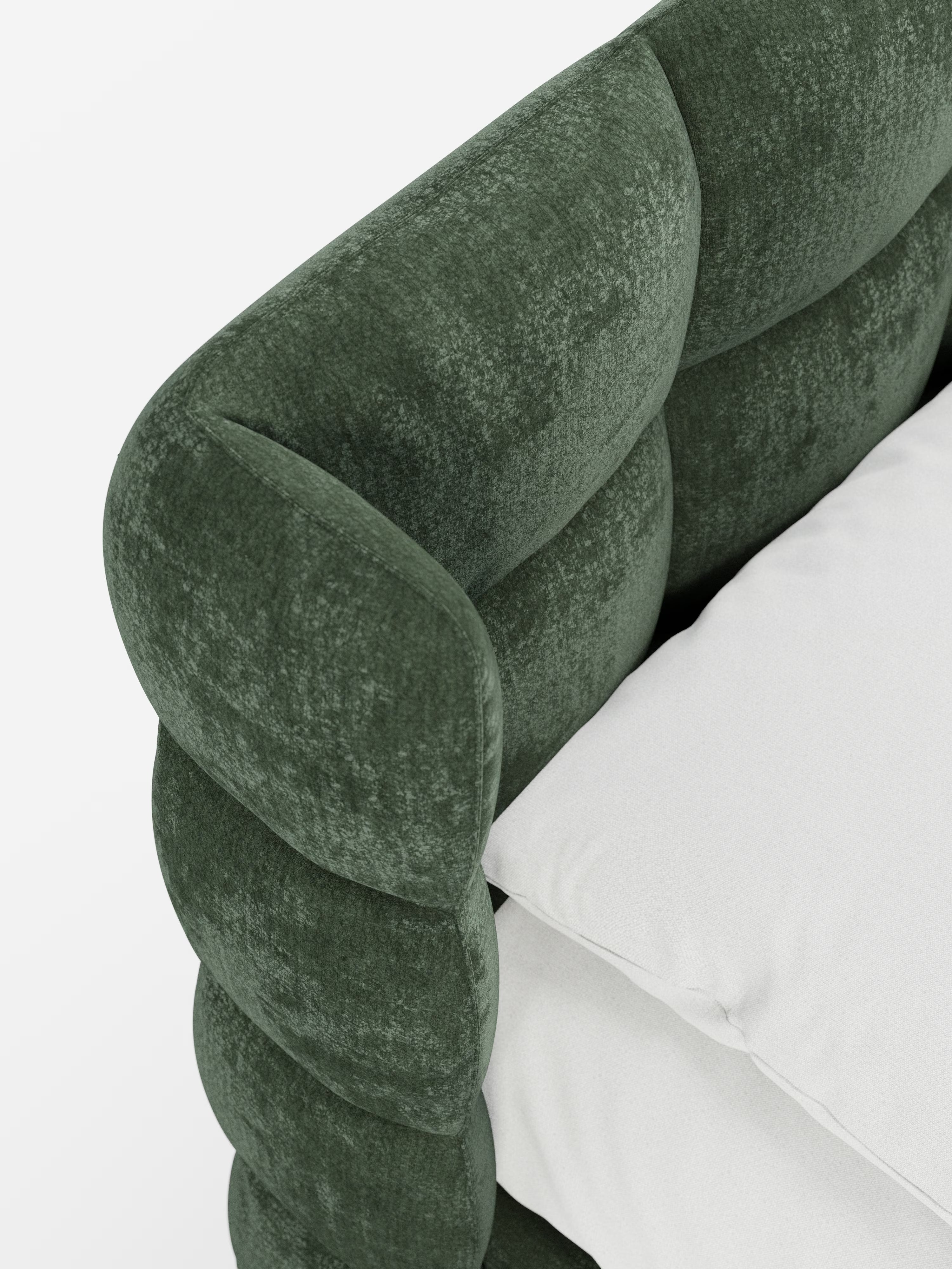 Primo piano del letto RAGNAR di Letti.store, che mette in risalto il suo tessuto verde intenso, certificato Oeko-Tex®, con un rivestimento testurizzato e trapuntato che ricorda una testiera capitonné. L'immagine si concentra sulla testiera morbida e avvolgente e sul bordo robusto e arrotondato. Un cuscino bianco e voluminoso poggia sulla seduta, mentre lo sfondo bianco a tinta unita mette in risalto la ricchezza del materiale e la morbidezza lussuosa di questo elegante letto contenitore.