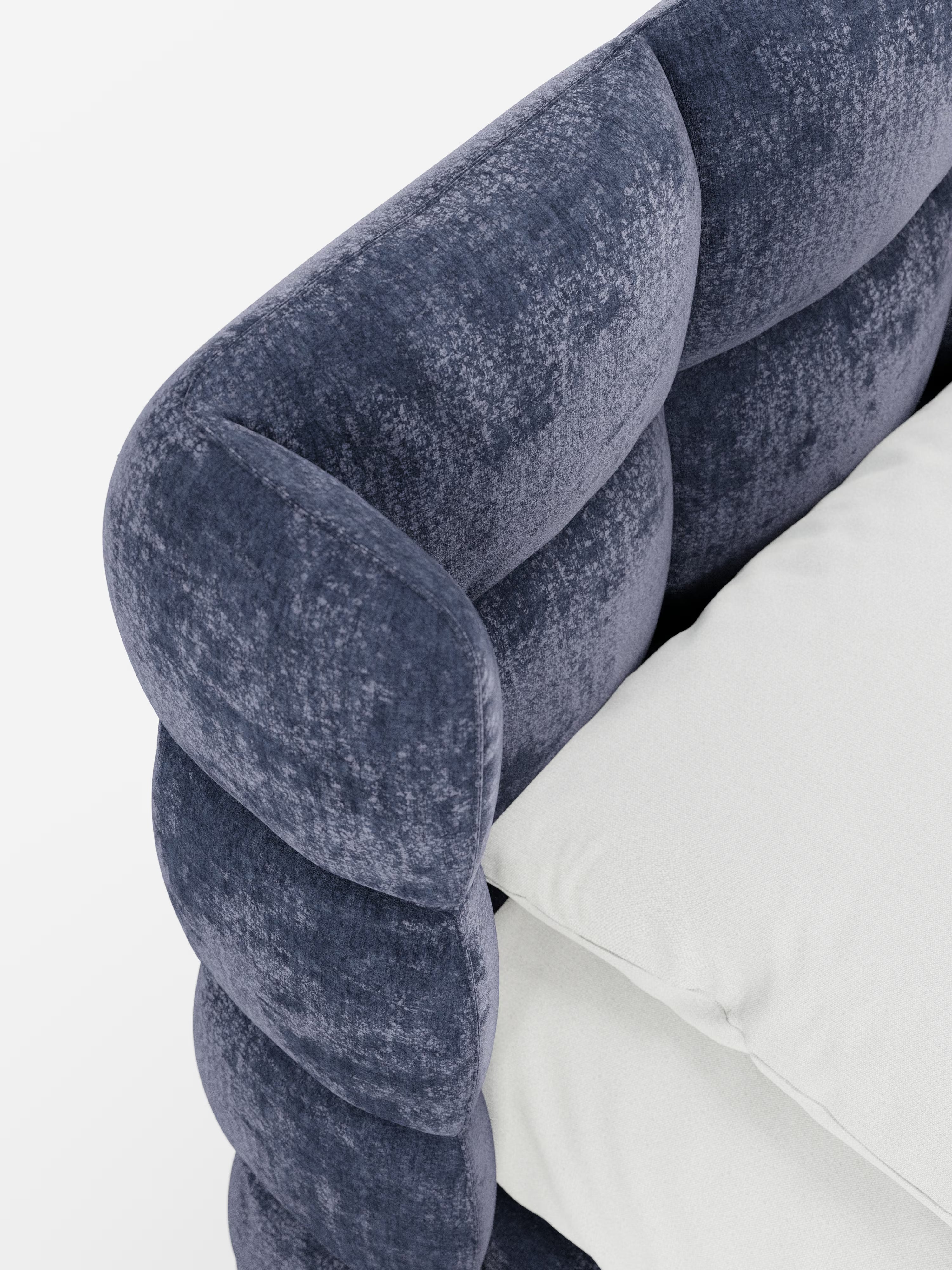 Primo piano del letto imbottito RAGNAR con contenitore e testiera capitonné avvolgente di Letti.store, rivestito in un morbido velluto blu intenso certificato Oeko-Tex®. Il design arrotondato e trapuntato dei braccioli richiama l’eleganza dell’artigianato italiano. Due cuscini color avorio poggiano sulla seduta, creando un splendido contrasto con la ricca trama del tessuto. Sullo sfondo bianco a tinta unita, risaltano i dettagli raffinati e la morbidezza lussuosa di questo modello di Letti.store.