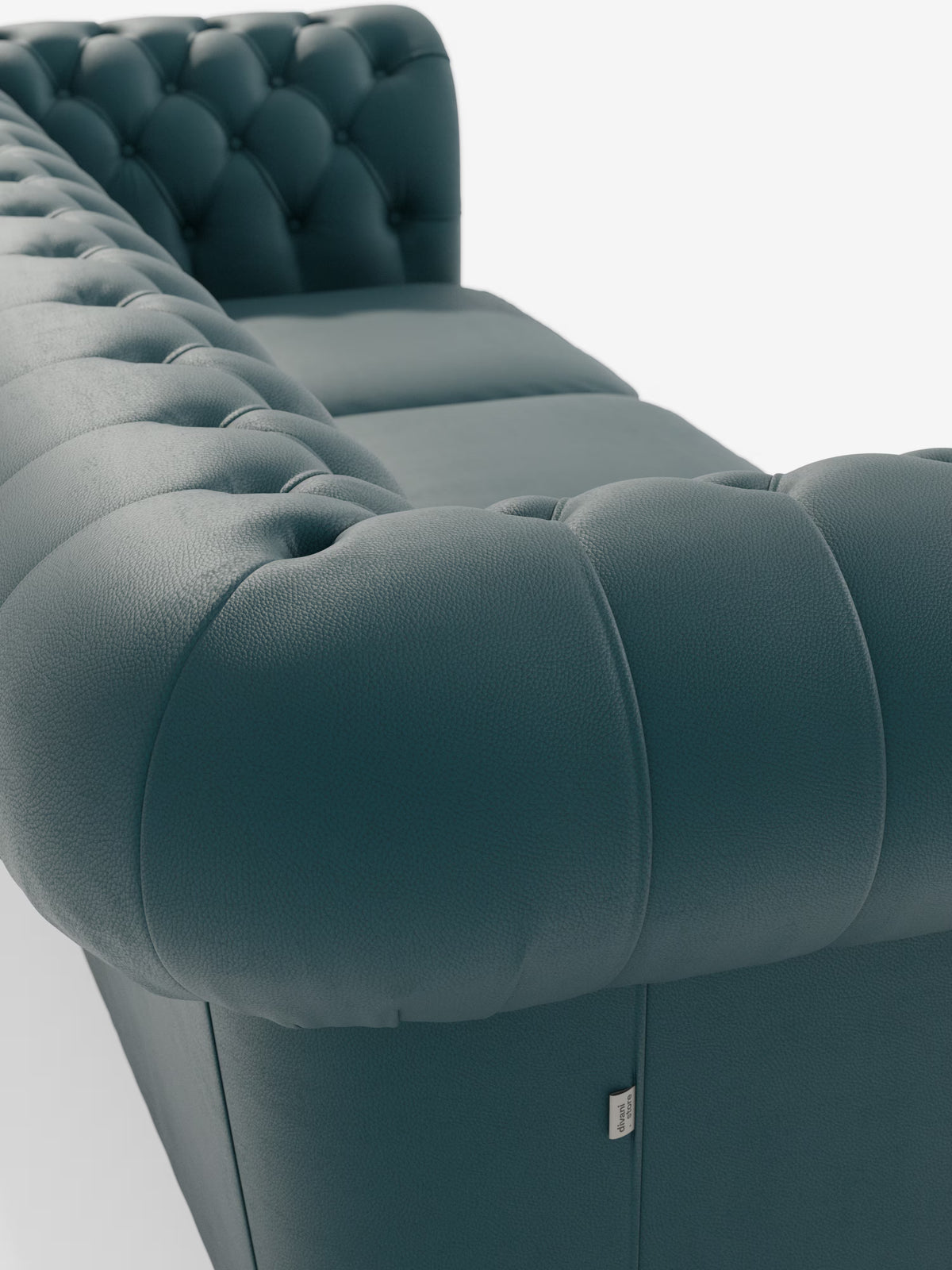 Primo piano del Chester 4 Posti 3 sedute in Vera Pelle – Chesterfield Capitonné Artigianale di Divani.Store, un divano in pelle color verde acqua scuro con finitura capitonné, caratterizzato da profondi bottoni decorativi e morbidi braccioli arrotondati. Realizzato con maestria in vera pelle di prima qualità e ispirato al classico stile Chesterfield, il divano mette in risalto la ricca trama della pelle. Una piccola etichetta in tessuto è applicata vicino alla base, su uno sfondo bianco a tinta unita.