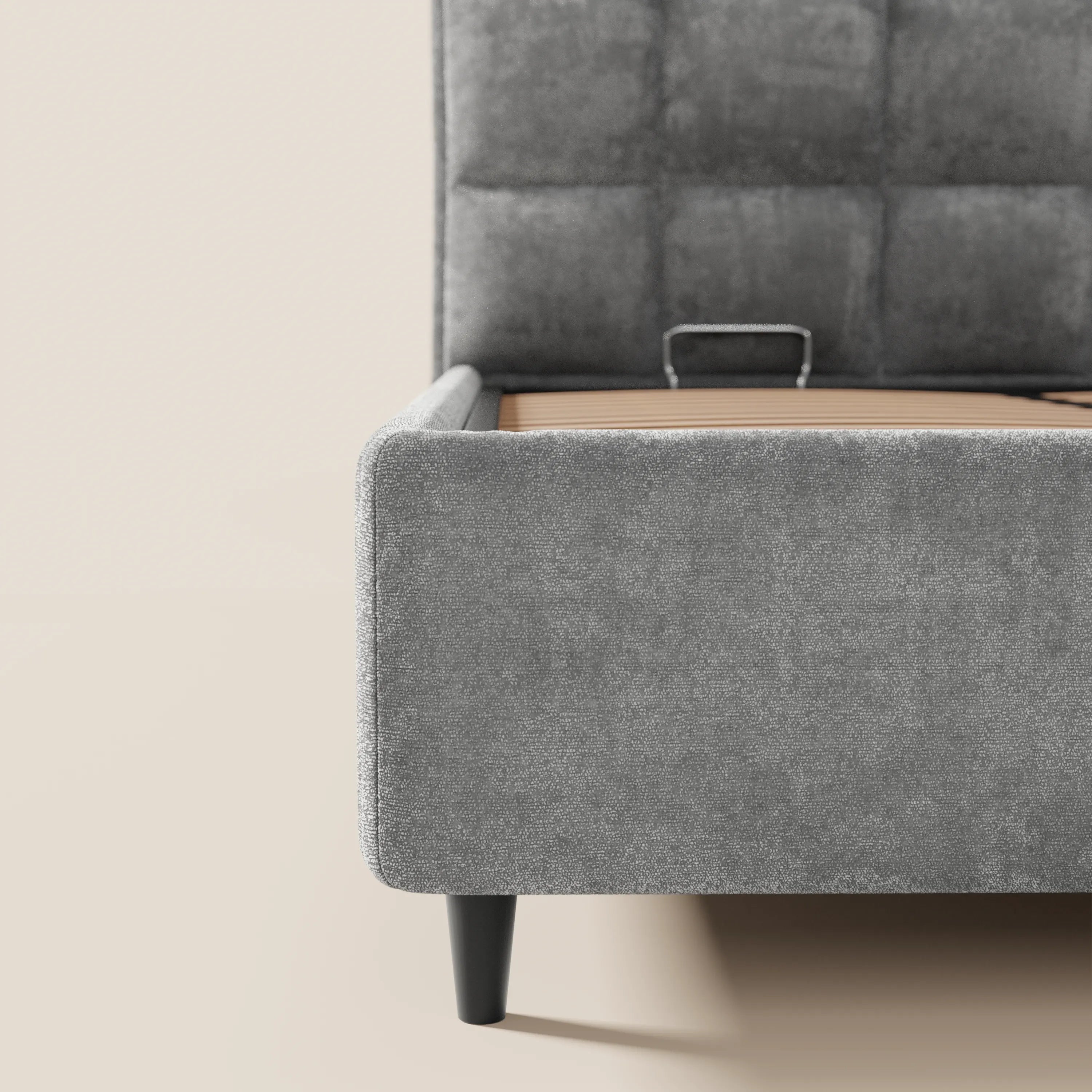 Un primo piano del letto imbottito AURO di Letti.store, caratterizzato da morbida ciniglia grigia certificata Oeko-Tex®, un’elegante testiera alta a quadri capitonné, gambe affusolate nere e un capiente contenitore, su un pavimento neutro in contrasto con una parete chiara.