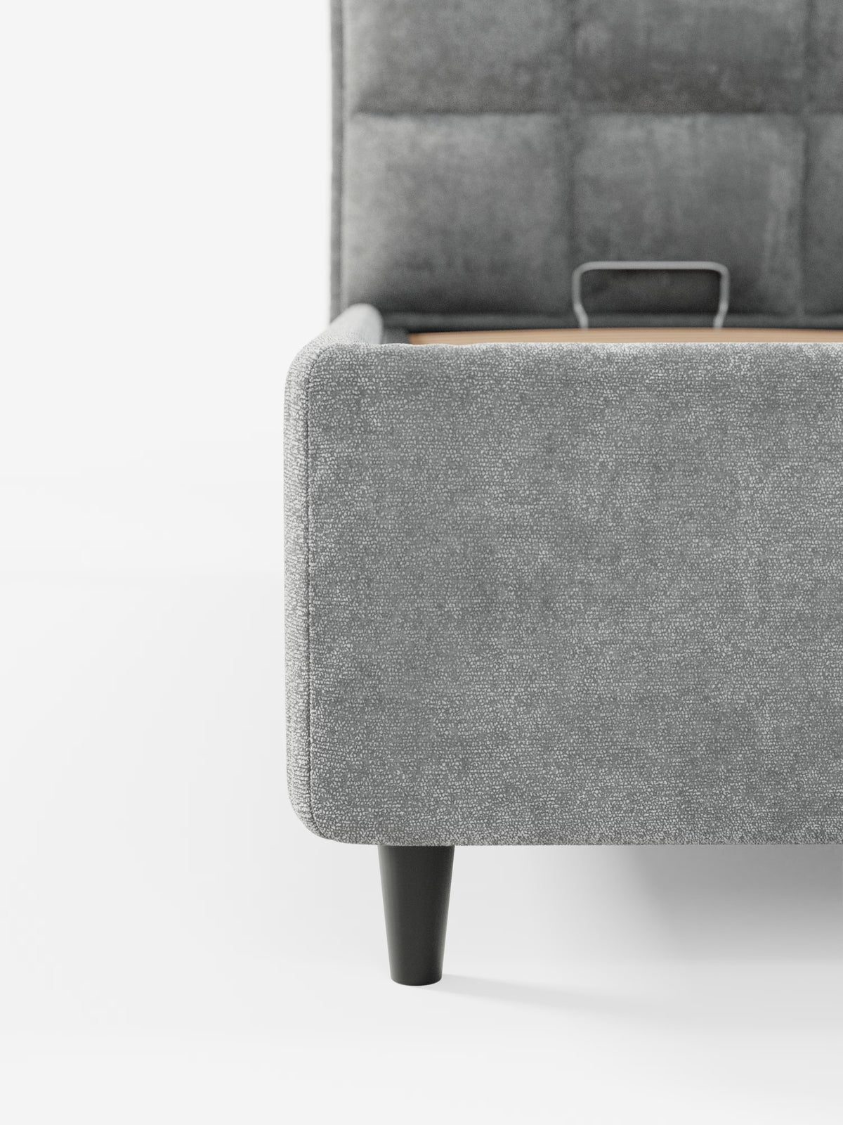 Un primo piano della base del letto imbottito AURO con vano contenitore e testiera capitonné alta in ciniglia Oeko-Tex® di Letti.store mette in risalto il rivestimento in ciniglia grigia che conferisce un aspetto morbido e ricco di texture. Le gambe angolate nere aggiungono un tocco di modernità, mentre la testiera alta presenta un motivo trapuntato a griglia: un’interpretazione contemporanea del classico stile capitonné. Lo sfondo è bianco a tinta unita.