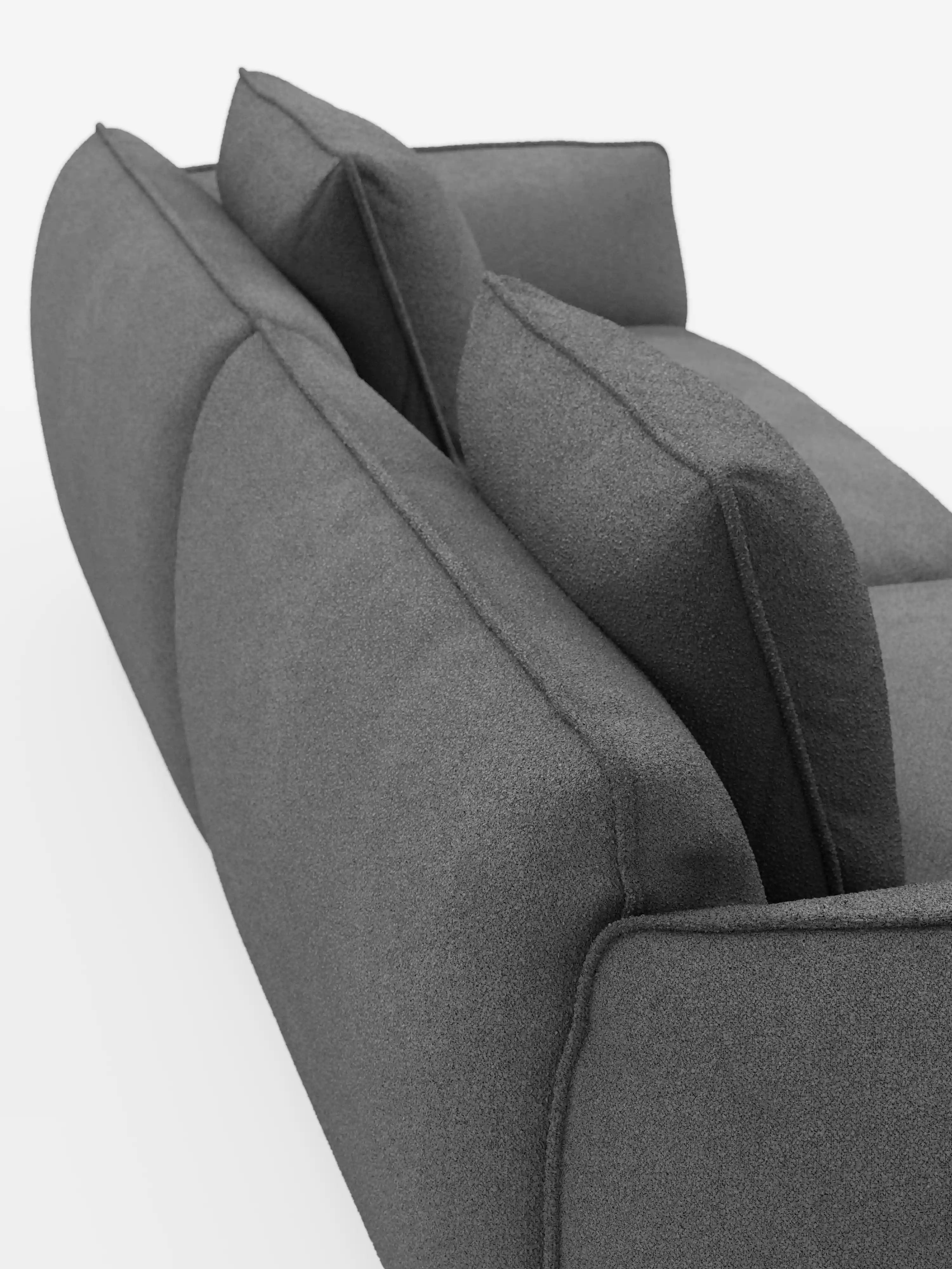 Un primo piano obliquo del divano Nimbus a 3 posti, modulare e componibile, da 250 cm di Divani.Store, in grigio scuro, caratterizzato da morbidi cuscini e due grandi cuscini dello schienale. Il divano, rivestito in tessuto sfoderabile effetto cotone antimacchia (t33), è fotografato su uno sfondo bianco che ne mette in risalto lo schienale e la parte superiore.