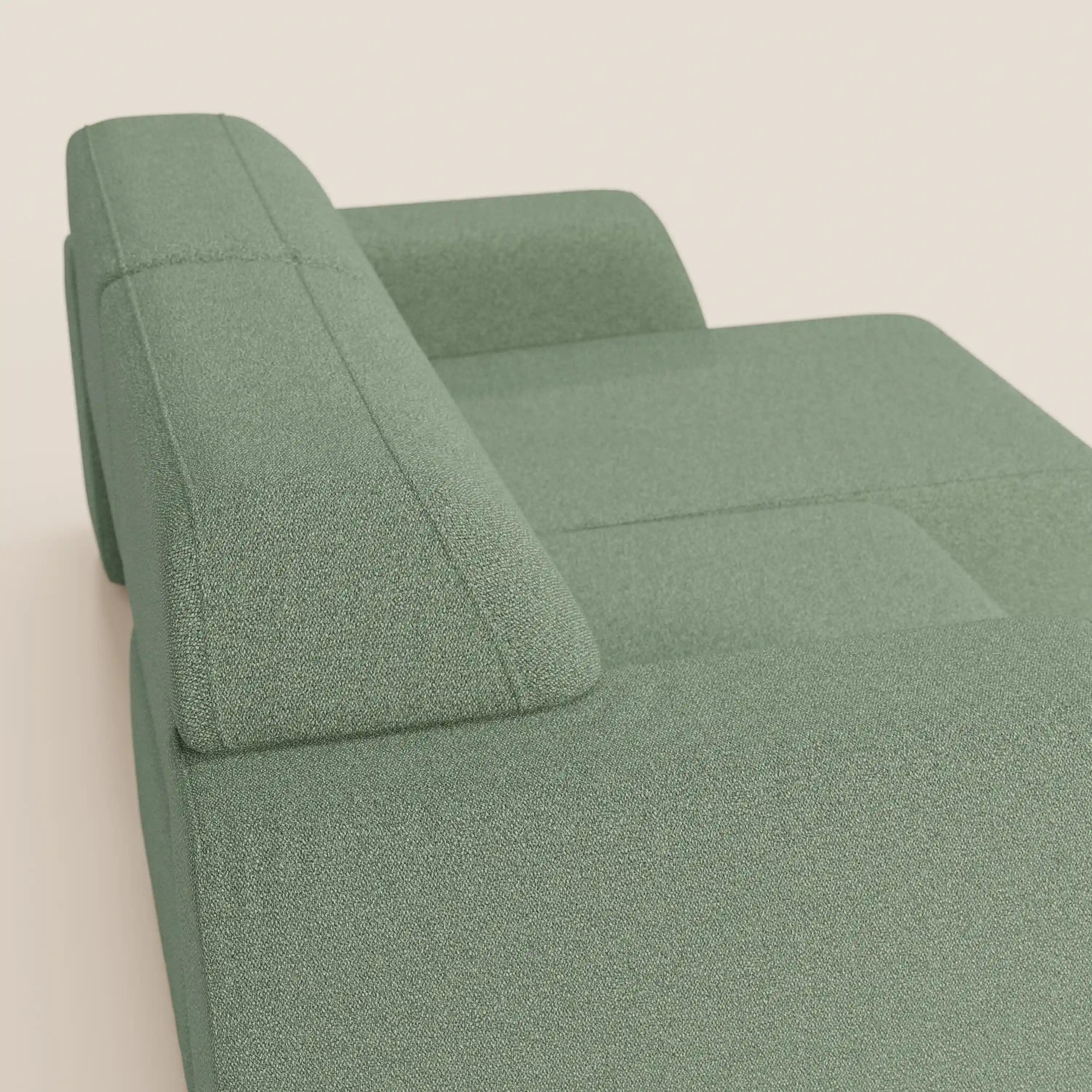 Una vista ravvicinata e angolata del divano Orbit 2 e 3 posti con sedute scorrevoli di Divani.Store, in tessuto verde chiaro smacchiabile effetto cotone T33, caratterizzato da ampi braccioli e schienale imbottiti su uno sfondo bianco sporco.