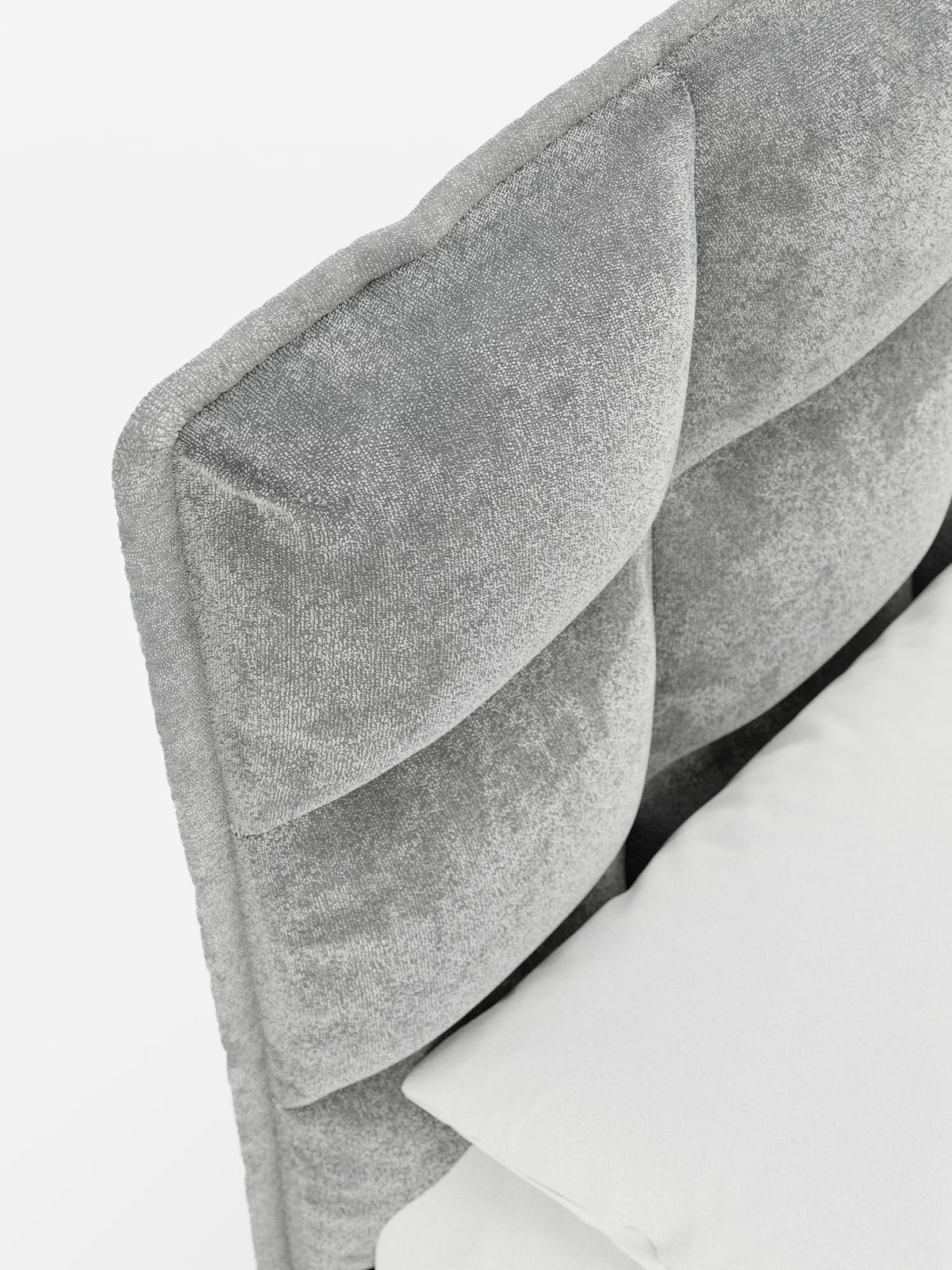 Primo piano del letto imbottito AURO di Letti.store, caratterizzato da una testiera alta con imbottitura soffice e lavorazione capitonné in morbida ciniglia certificata Oeko-Tex®. Il rivestimento grigio testurizzato emana eleganza, mentre un angolo di un cuscino bianco poggia contro la testiera. Su uno sfondo bianco, le linee pulite e il design personalizzabile di questo letto lo rendono perfetto per gli interni contemporanei.