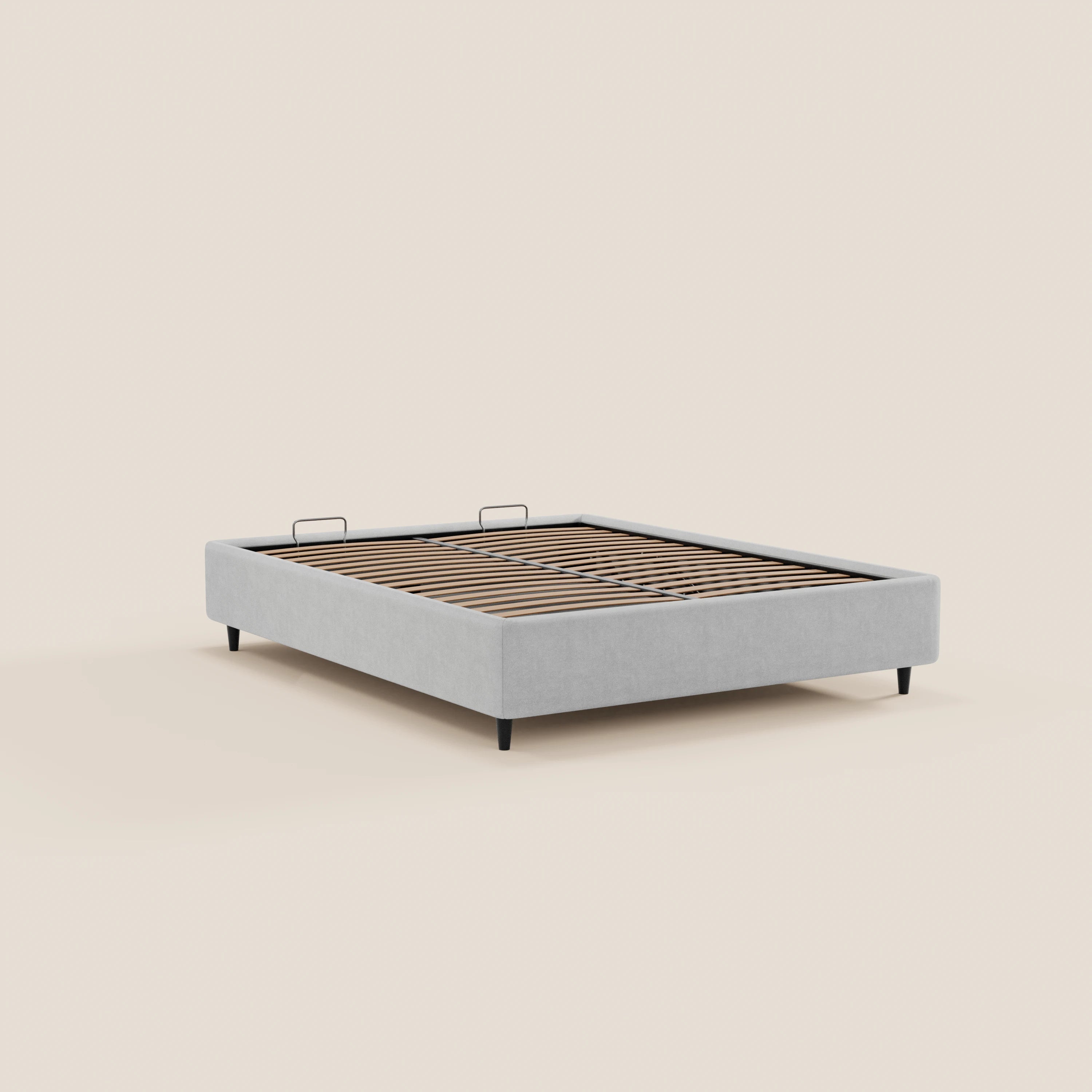 Il letto sommier imbottito ERON di Letti.store è realizzato in tessuto impermeabile Oeko-Tex grigio chiaro, con gambe angolate nere, doghe in legno e due piccole maniglie metalliche. Nell’immagine è raffigurato senza materasso su uno sfondo beige a tinta unita.