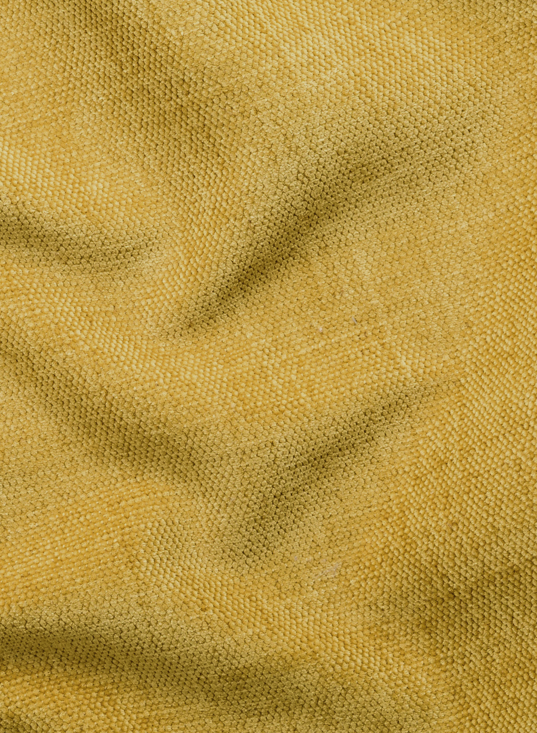 Un primo piano di un tessuto intrecciato, dalla trama ruvida, color giallo senape, su un divano Ischia a 3 posti con pouf estraibile e schienali traslanti in tessuto misto lino smacchiabile, che mostra delicate pieghe e giochi di luce che ne esaltano la superficie morbida e soffice.