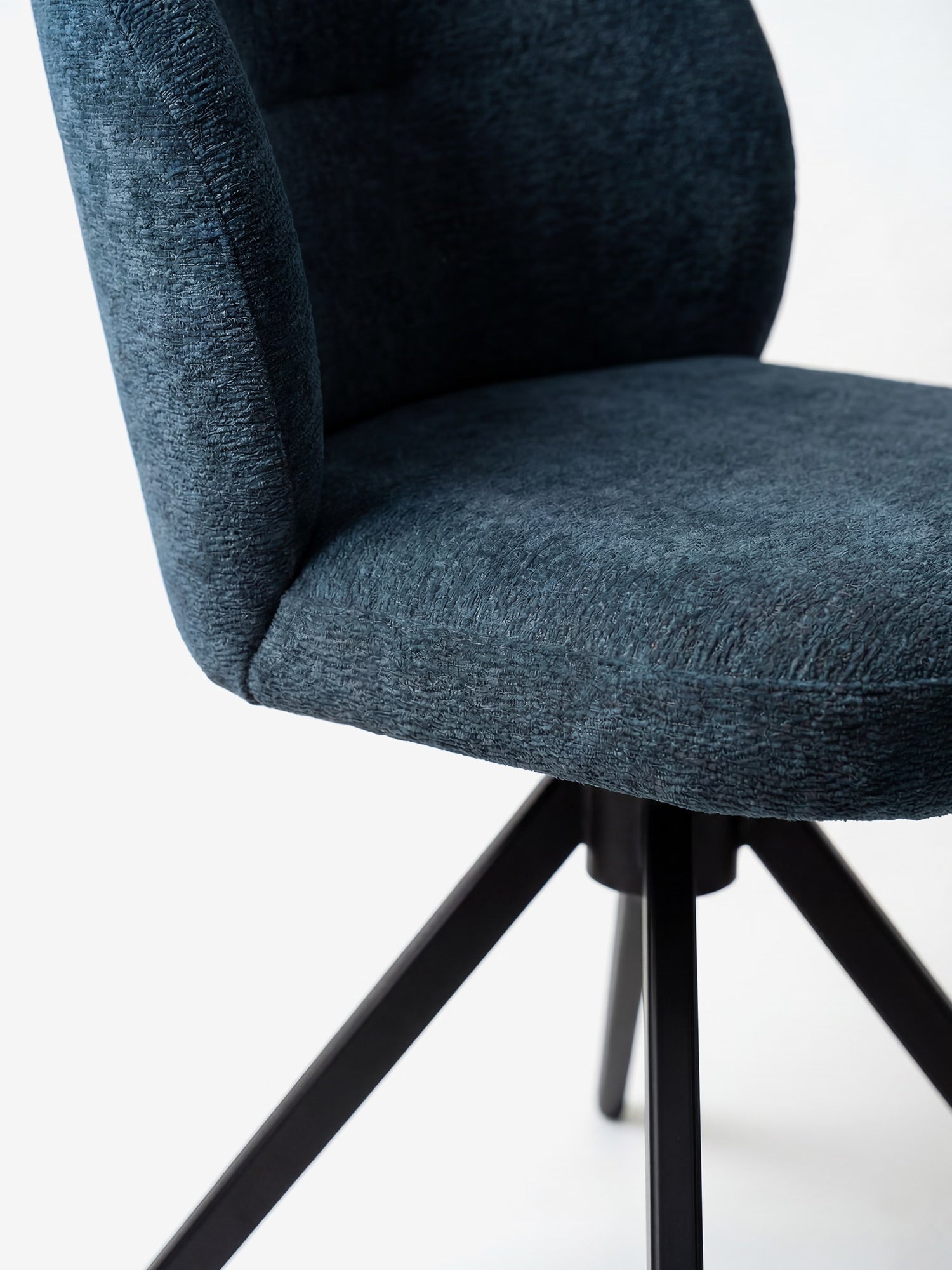 Primo piano della sedia Alba di Divani.Store, realizzata con tessuto effetto cotone certificato OEKO-TEX® in blu scuro e dotata di schienale curvo e gambe divaricate in metallo nero. Solo una parte di questa elegante sedia è visibile su uno sfondo bianco a tinta unita.