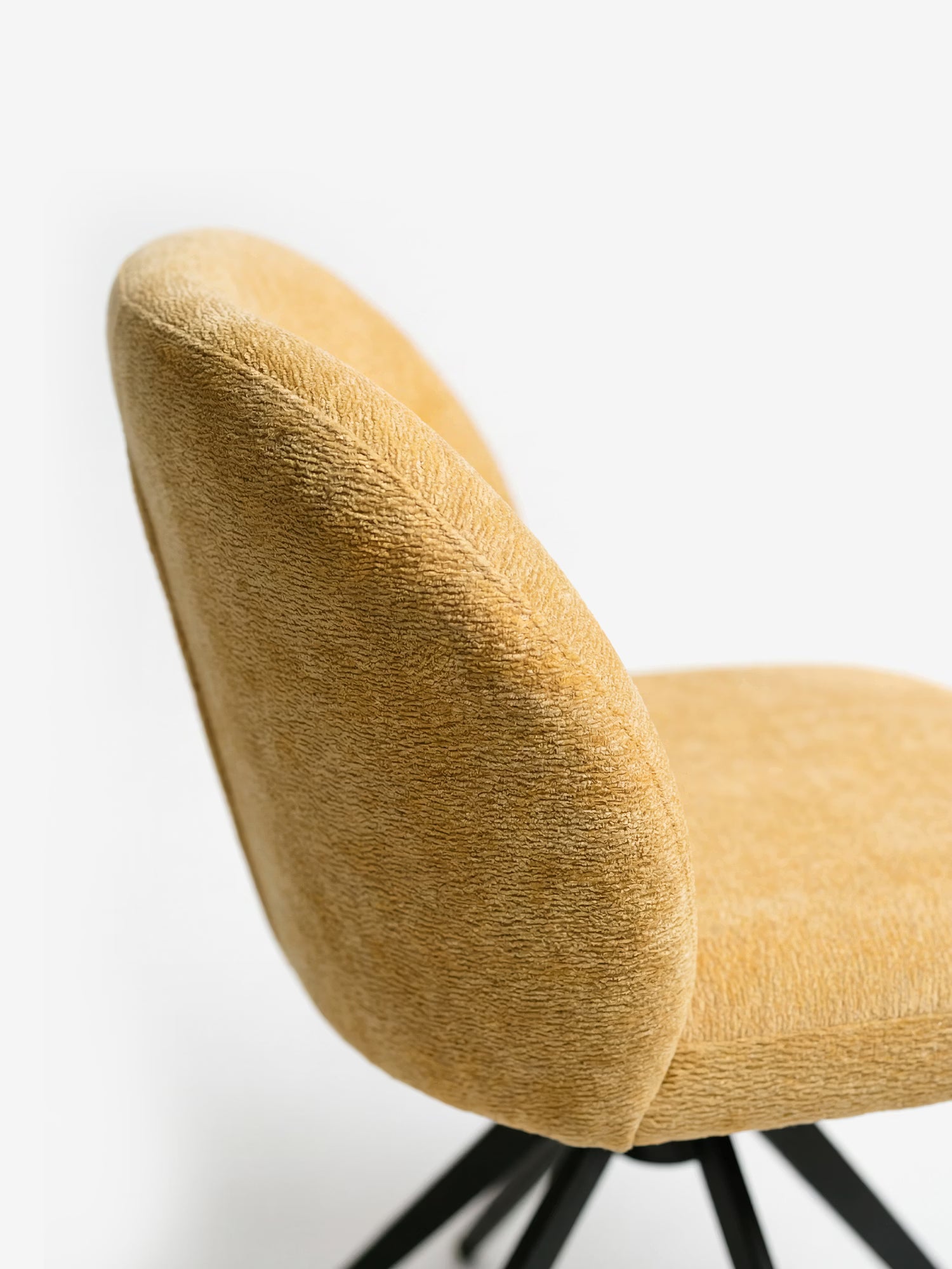 Una vista laterale ravvicinata della sedia imbottita Alba in tessuto effetto cotone certificato OEKO-TEX® di Divani.Store, caratterizzata da schienale e seduta arrotondati su gambe in metallo nero, ne mette in risalto il design moderno e accogliente su uno sfondo bianco a tinta unita.