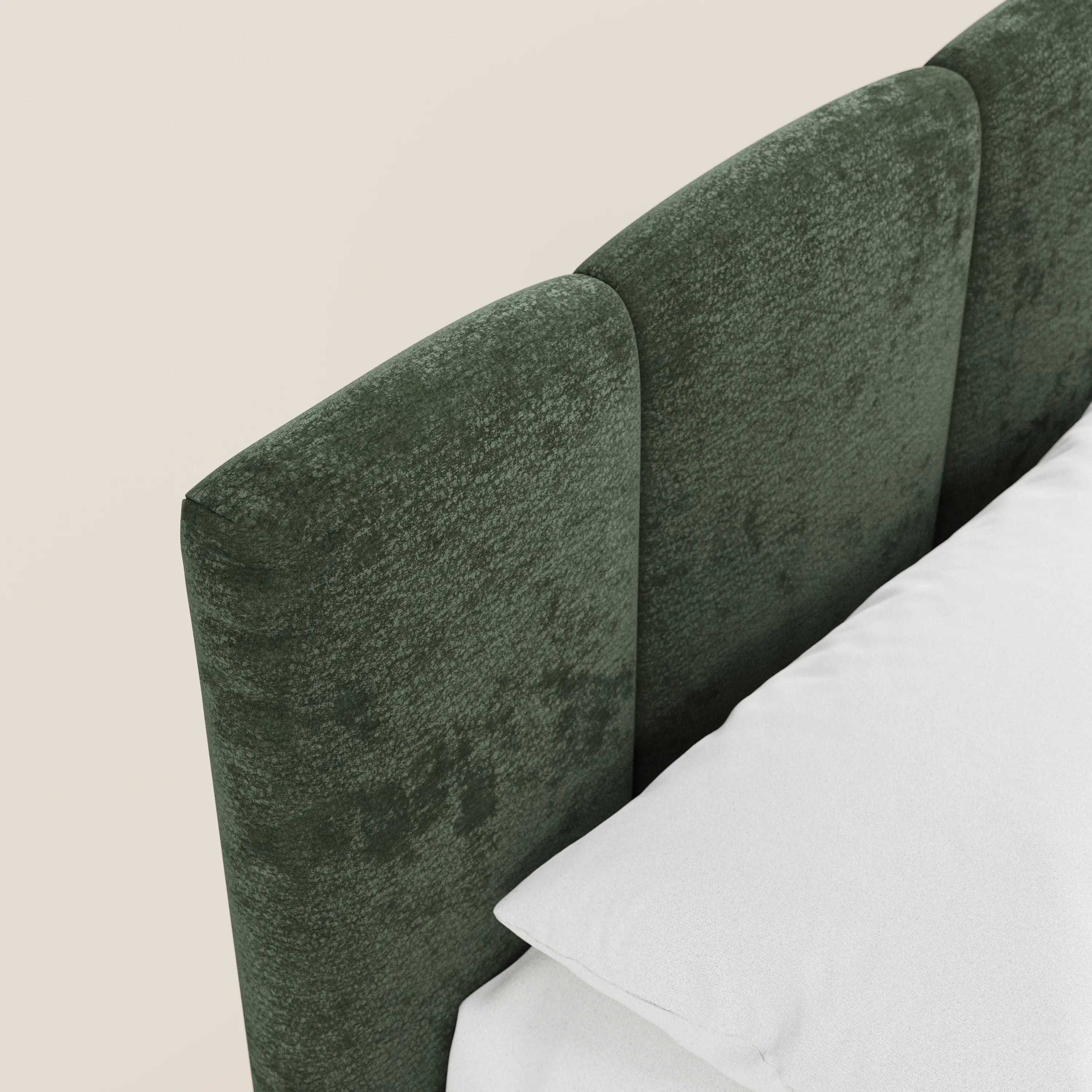 Primo piano del letto imbottito ARKAM di Letti.store, caratterizzato da una testiera in tessuto verde certificato Oeko-Tex® con pannelli verticali e vano contenitore integrato. Il letto è sistemato con cura contro una parete chiara, mettendo in risalto il suo design shabby chic.