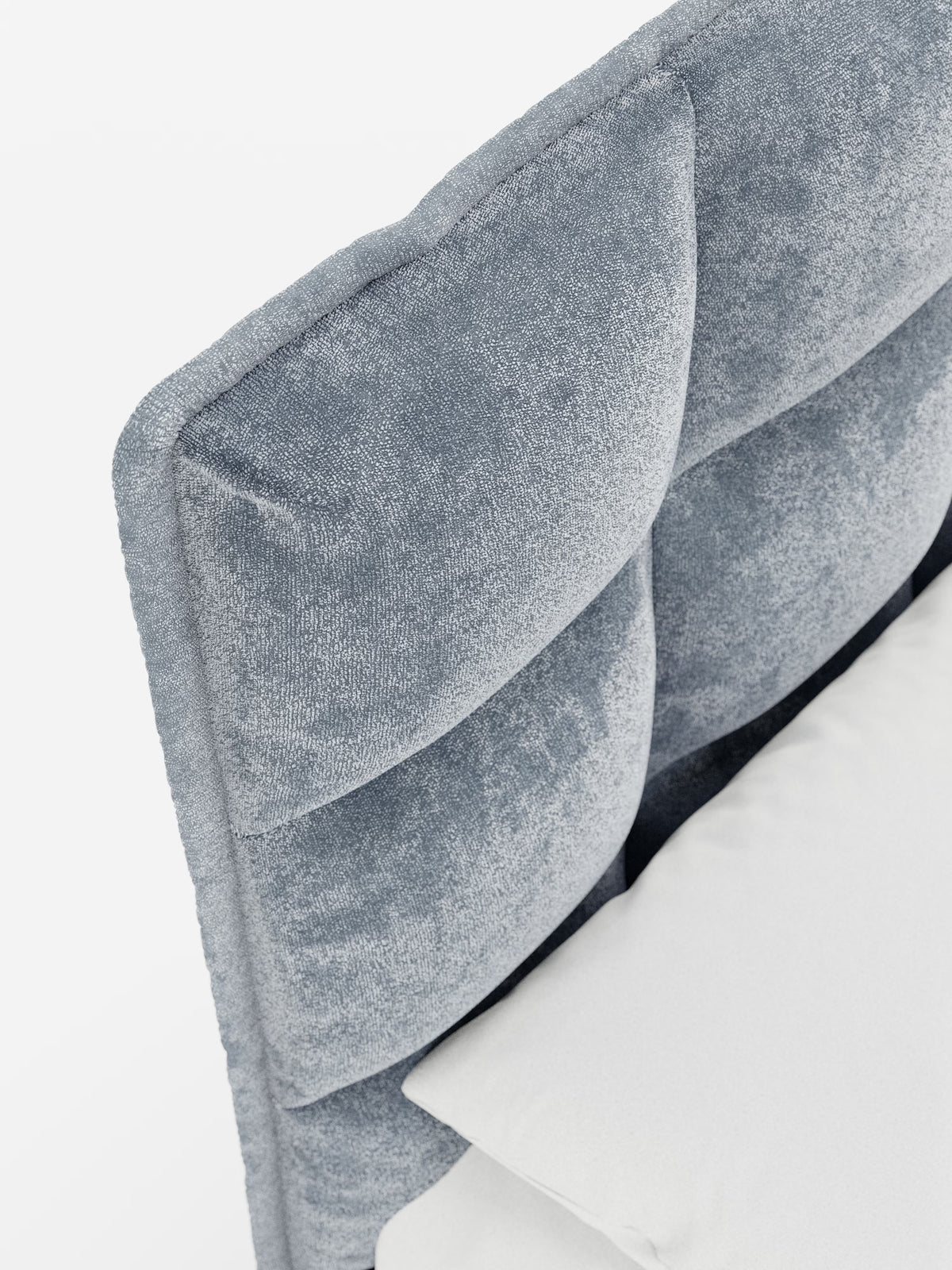 Primo piano del letto imbottito AURO con contenitore e testiera alta capitonné in ciniglia Oeko-Tex® di Letti.store, che mette in risalto la sua testiera alta capitonné rivestita in morbida ciniglia azzurra dalla trama ricca. Le ampie e morbide sezioni rettangolari esaltano l’estetica moderna, in contrasto con il cuscino e le lenzuola di un bianco candido. Lo sfondo bianco a tinta unita mette in risalto i materiali pregiati e la maestria artigianale del letto.