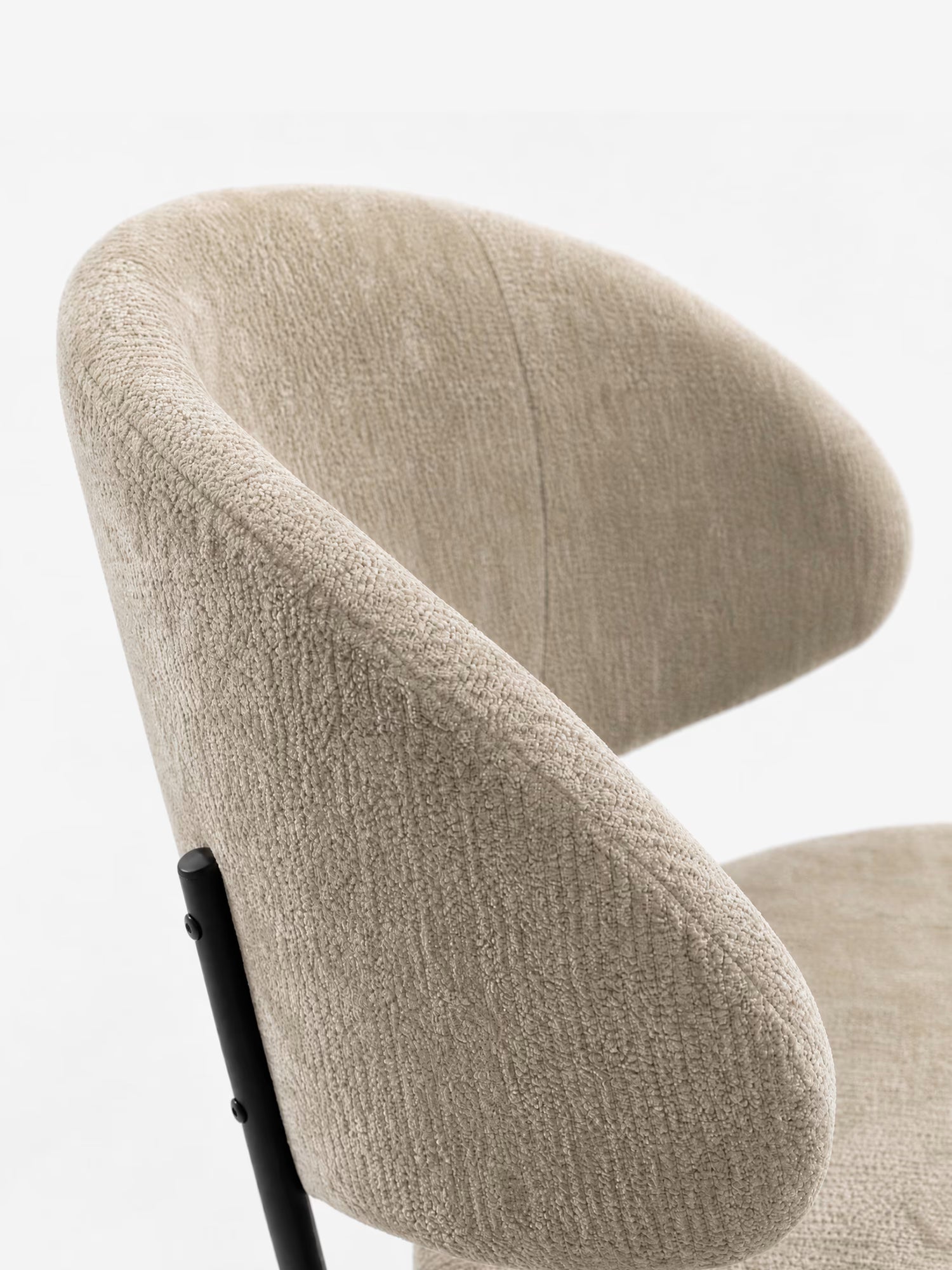 Primo piano della sedia Bruma di Divani.Store, caratterizzata da un elegante tessuto goffrato color beige e da gambe in metallo nero. Il design minimalista con lo schienale avvolgente risalta su uno sfondo bianco a tinta unita.