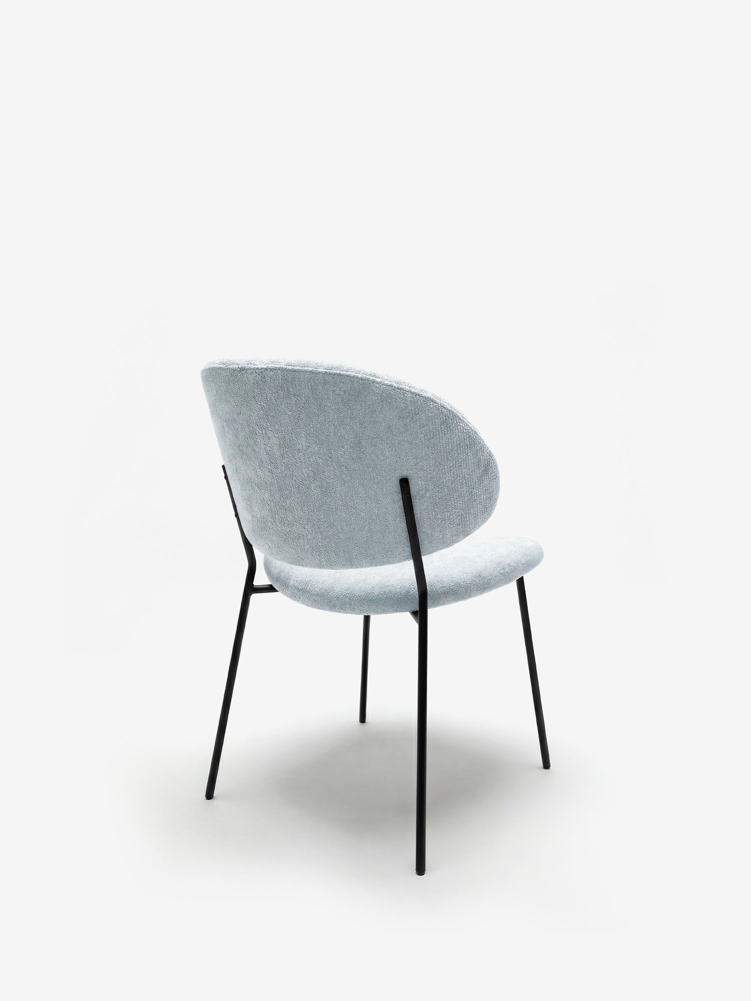 La Bruma di Divani.Store è una sedia dal design minimalista: elegante tessuto goffrato grigio chiaro, schienale avvolgente e curvo e seduta imbottita, sostenuta da quattro gambe nere in metallo. Ripresa di spalle su sfondo bianco.