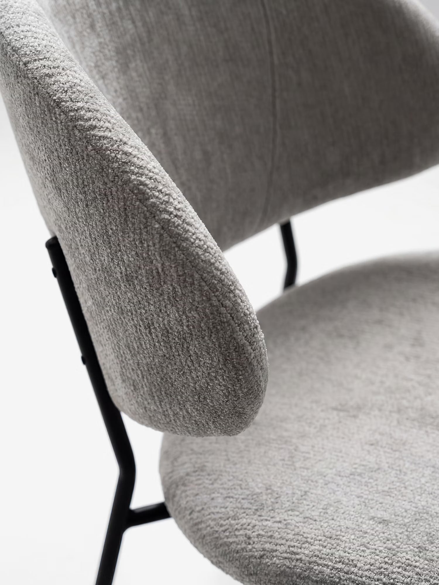 Primo piano della sedia Bruma di Divani.Store: elegante tessuto goffrato chiaro, schienale avvolgente e linee minimaliste con gambe e braccioli in metallo nero, su sfondo bianco.