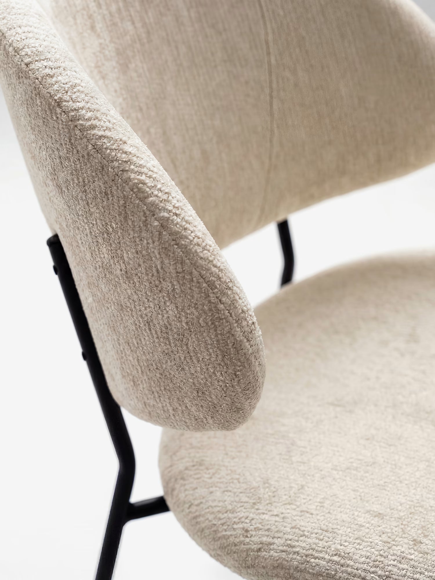 Primo piano della sedia Bruma di Divani.Store, caratterizzata da un elegante tessuto goffrato color beige, uno schienale avvolgente imbottito e gambe minimaliste in metallo nero, per un look chic su sfondo bianco.