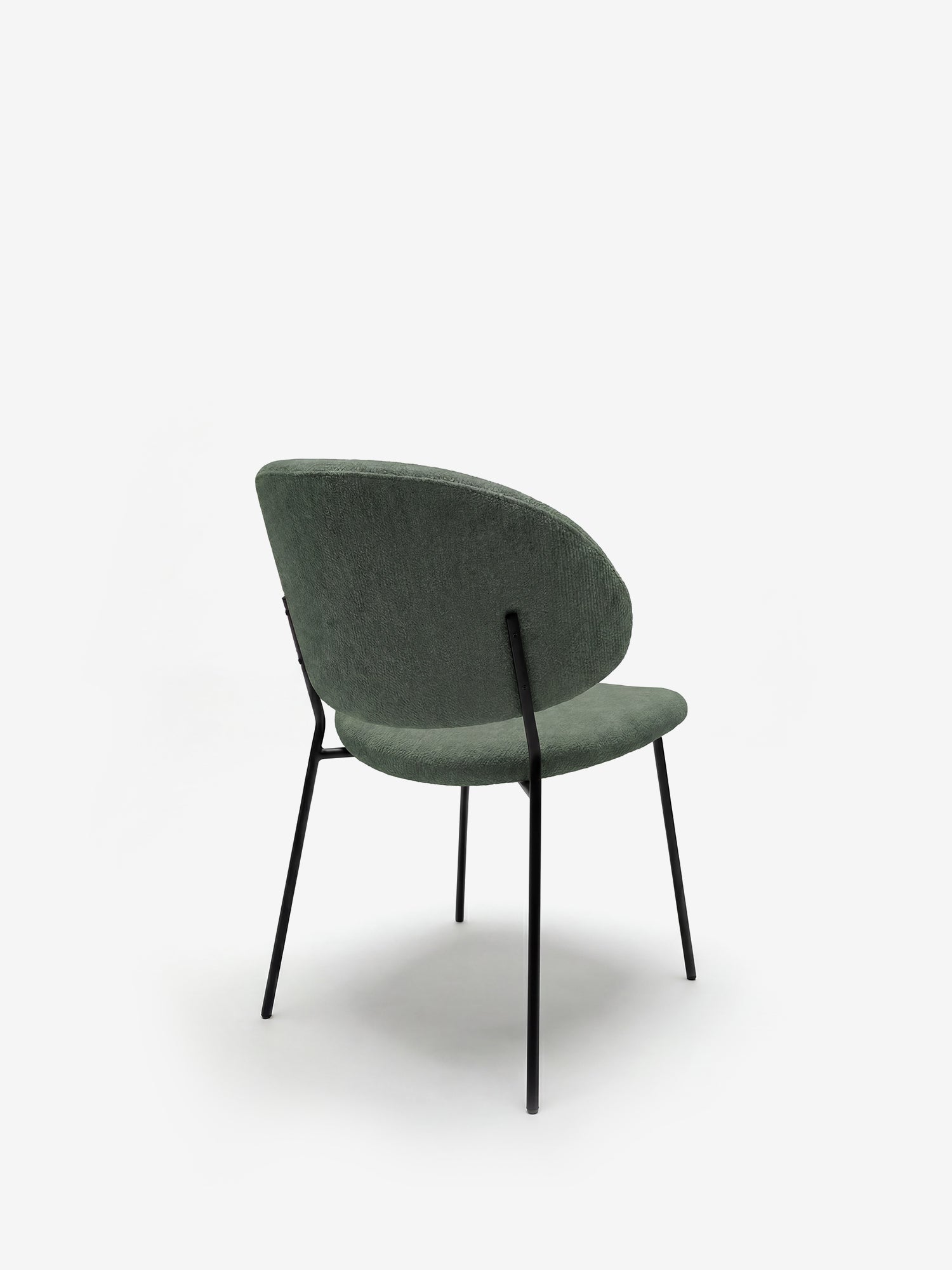 La sedia Bruma di Divani.Store presenta un design minimalista con uno schienale avvolgente in elegante tessuto goffrato verde e sottili gambe in metallo nero, raffigurata di spalle in controluce su uno sfondo bianco a tinta unita.
