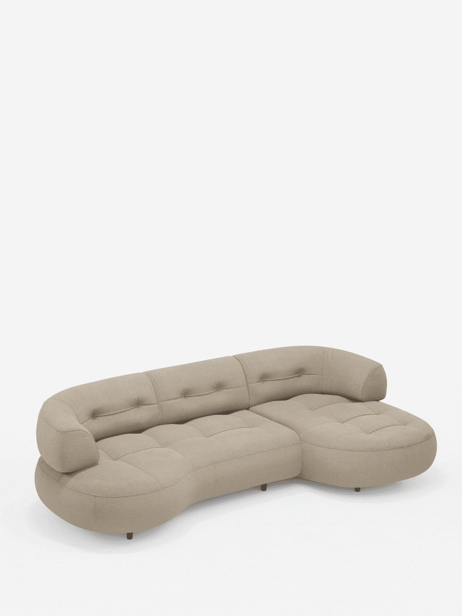 Un divano angolare Croissant dalla forma ricurva a fagiolo, con schienali scorrevoli in morbido tessuto effetto cotone smacchiabile T33 color beige chiaro, si staglia su uno sfondo bianco con dettagli trapuntati e braccioli arrotondati.