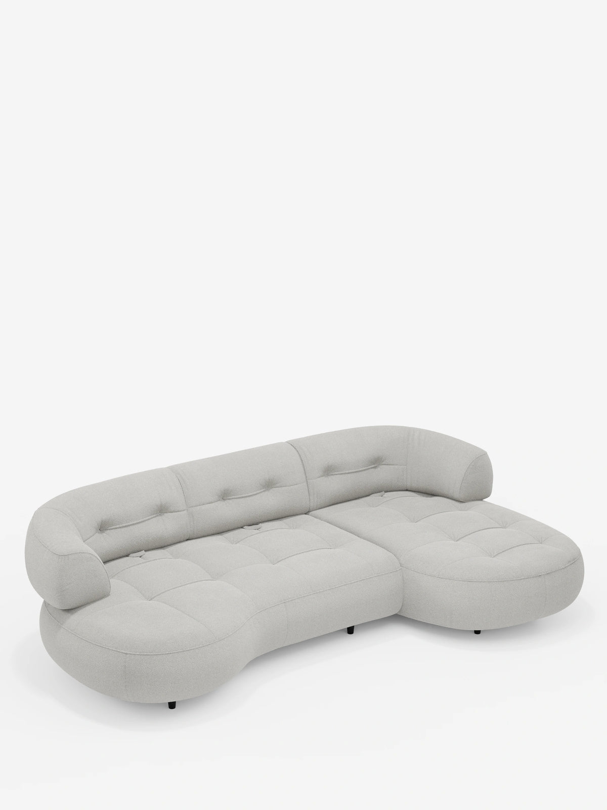 Un divano angolare Croissant di colore grigio chiaro, dal design a forma di fagiolo e con schienali scorrevoli, rivestito in morbido tessuto effetto cotone smacchiabile T33, si staglia su uno sfondo bianco con cuscini trapuntati dal profilo basso e piccole gambe nere.