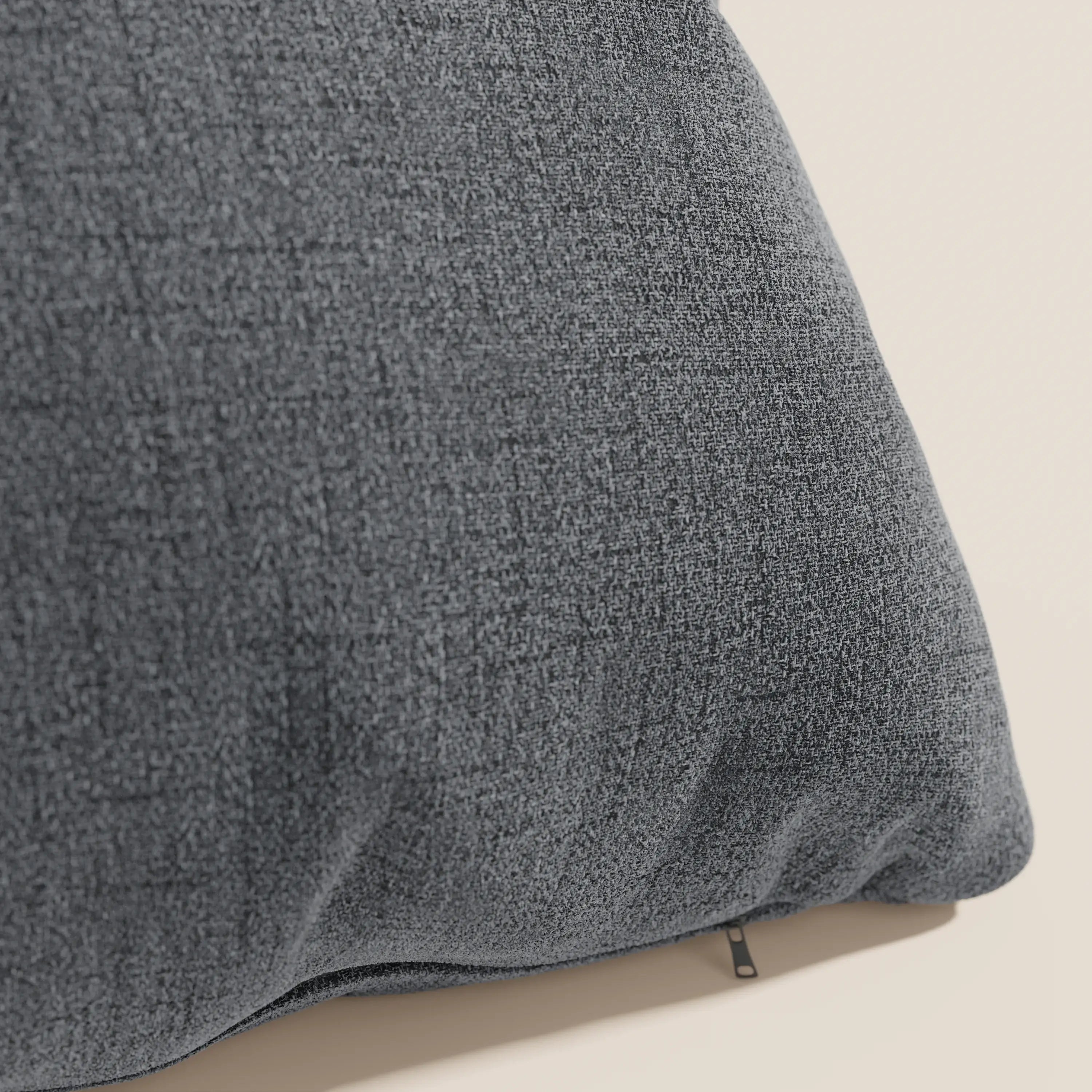 Un primo piano del cuscino Felis di Divani.Store, in tessuto morbido impermeabile T03 grigio, mostra il suo tessuto strutturato su uno sfondo beige con un angolo focalizzato e un piccolo tiretto nero sul bordo inferiore.