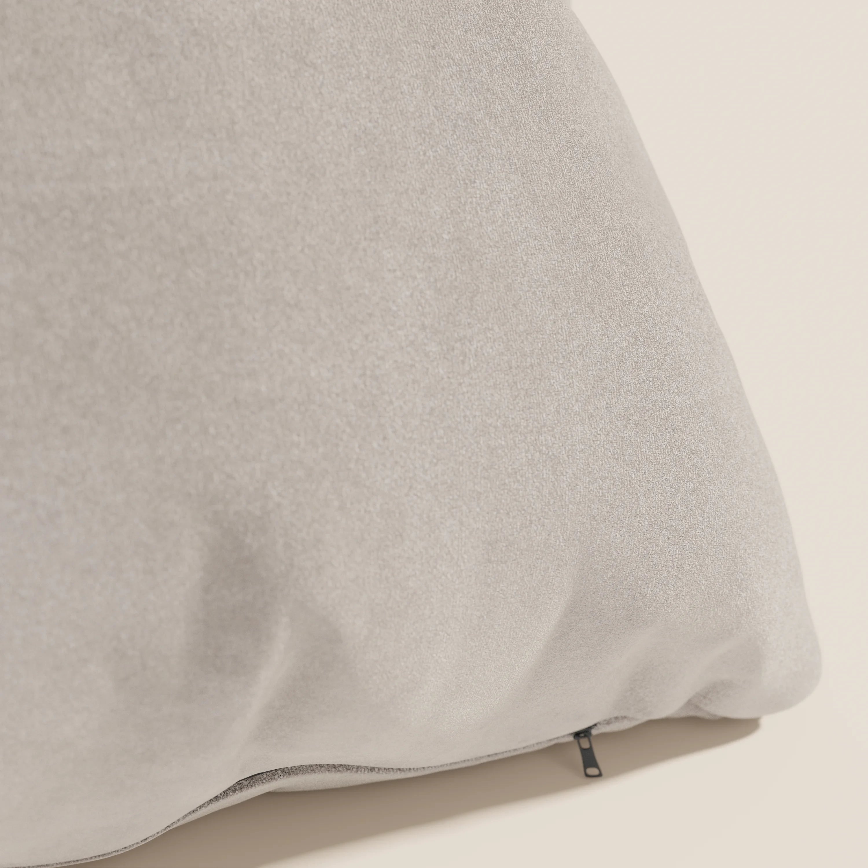 Primo piano del cuscino Jazz 45x45 di Divani.Store, in microfibra tecnica smacchiabile T11 tortora. Il cuscino grigio chiaro poggia su una superficie beige, con una piccola cerniera nera sul fondo che lascia intravedere un rivestimento sfoderabile.