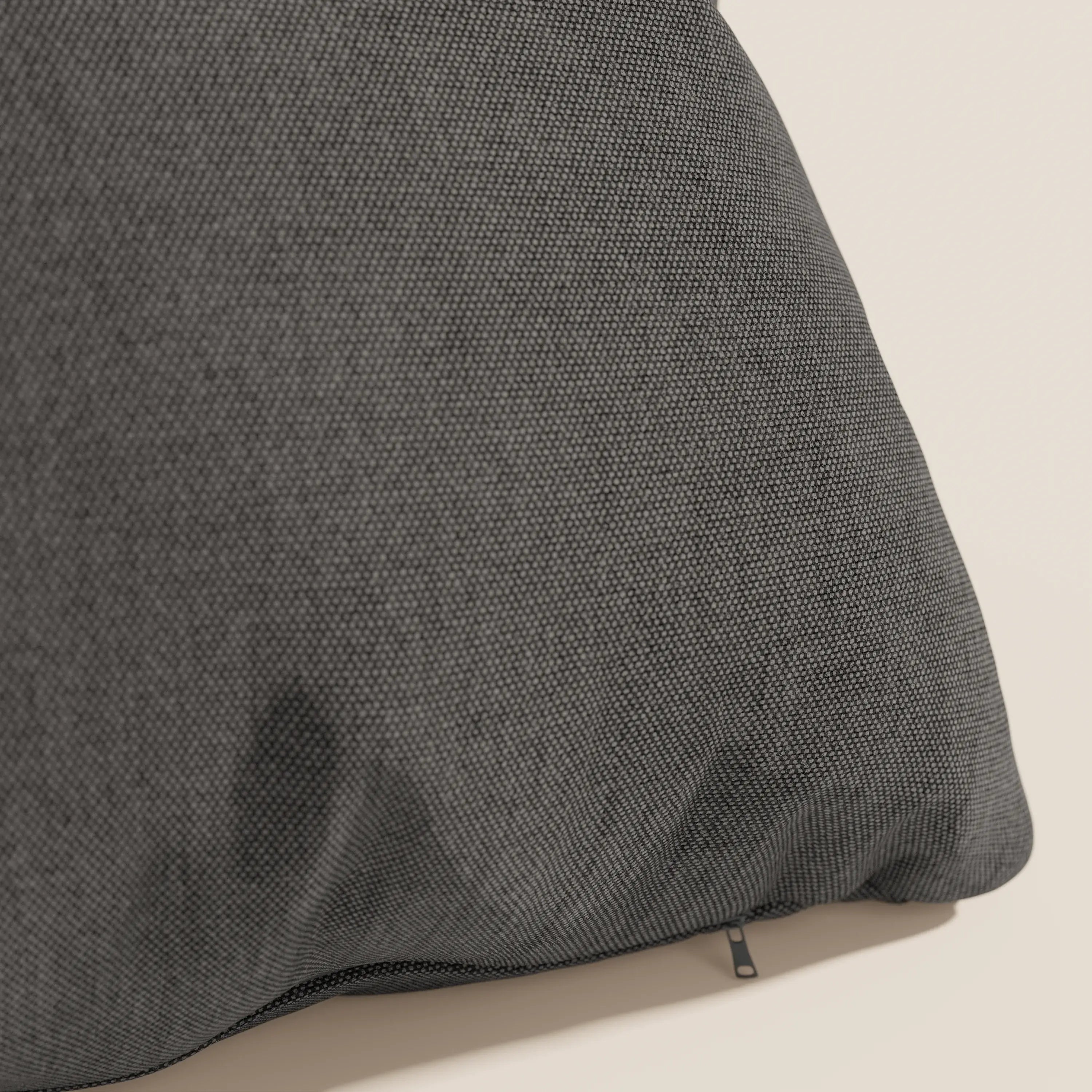 Primo piano del cuscino Honey 45x45 di Divani.Store in tessuto simil cotone impermeabile T13 antracite, su sfondo beige. Sul bordo è visibile una piccola cerniera nera, con una debole macchia scura sulla fodera inferiore lavabile.