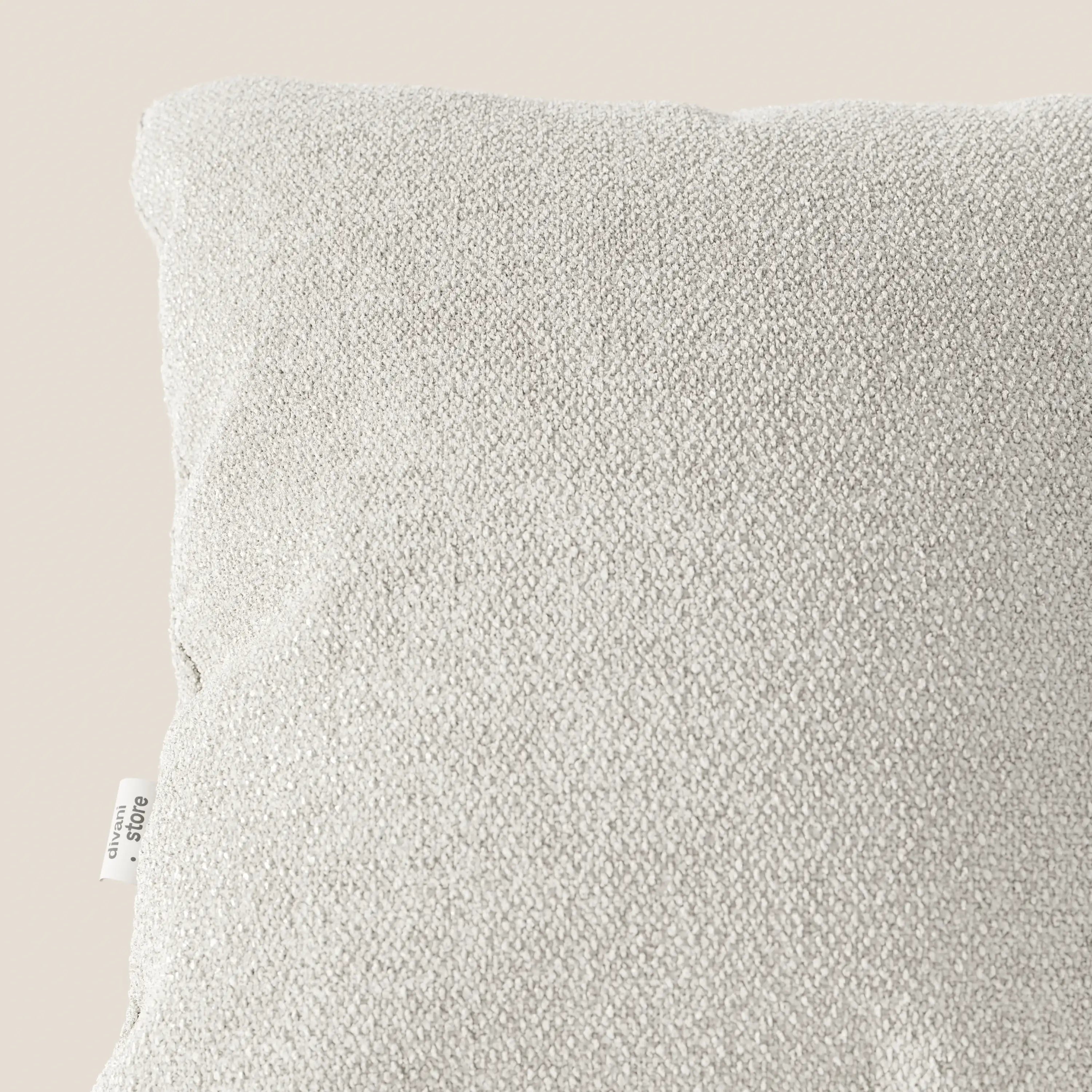 Primo piano del cuscino Lambada di Divani.Store, in tessuto smacchiabile tipo cotone T33 grigio chiaro, su sfondo beige. La cucitura del cuscino presenta una piccola etichetta bianca con testo nero; è mostrata solo una parte del cuscino.
