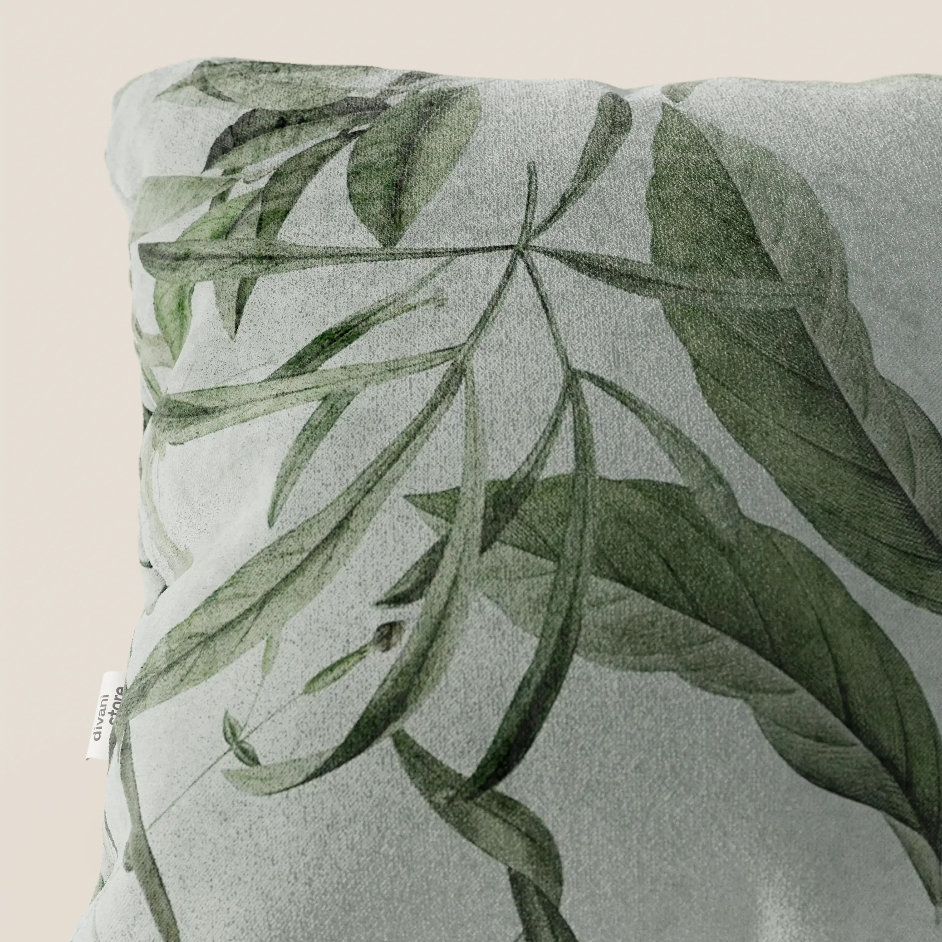 The Lemon elegante cuscino a fantasia in velluto impermeabile verde di Divani.Store presenta un motivo botanico di foglie verdi sovrapposte su sfondo grigio chiaro, con etichetta bianca sul lato e fondo beige.