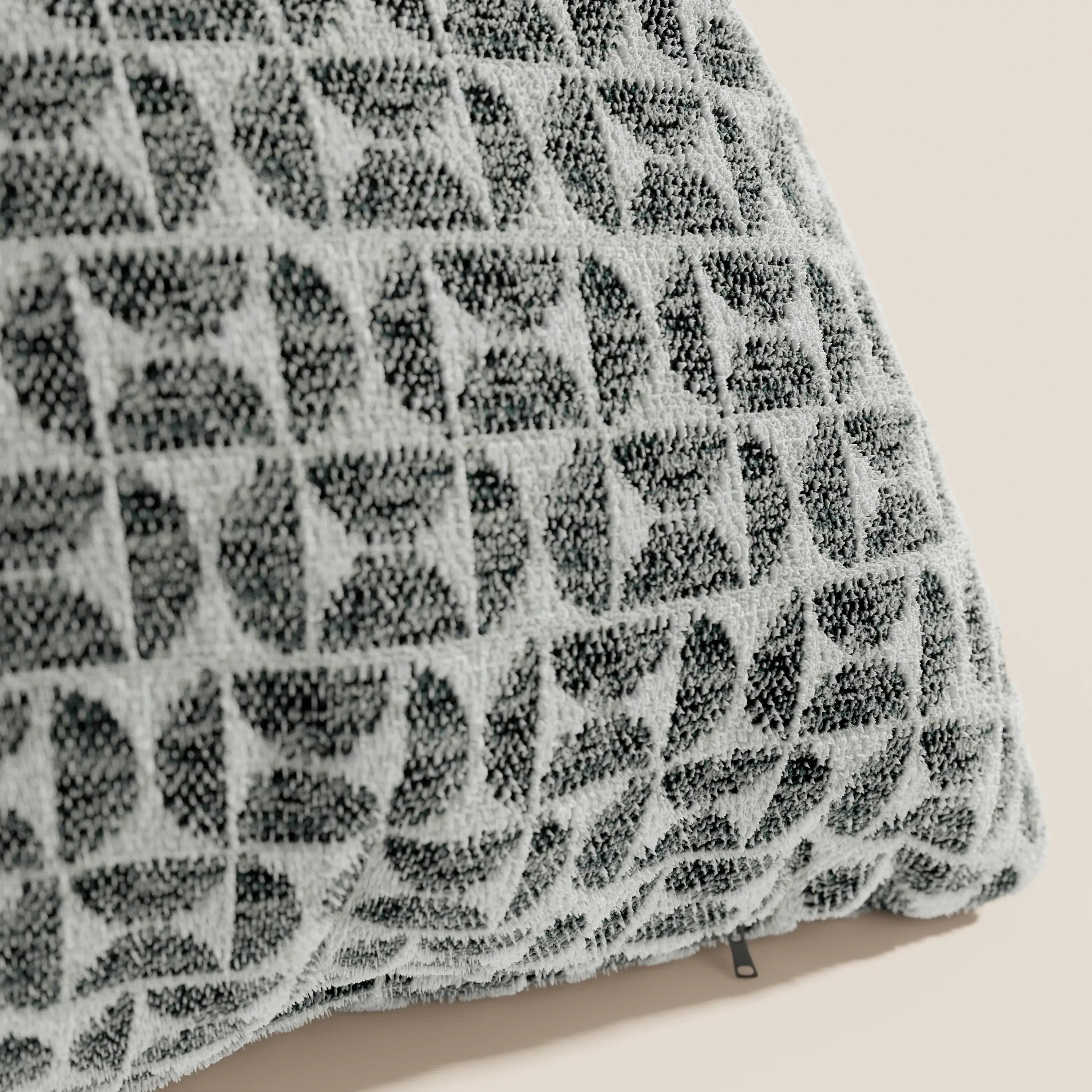 Primo piano del cuscino Naxos Decoro 45x45 in lino di Divani.Store, caratterizzato da un elegante motivo geometrico nei toni del grigio e del nero. Il cuscino poggia su una superficie unita color beige chiaro, con una piccola etichetta in tessuto sul bordo inferiore.