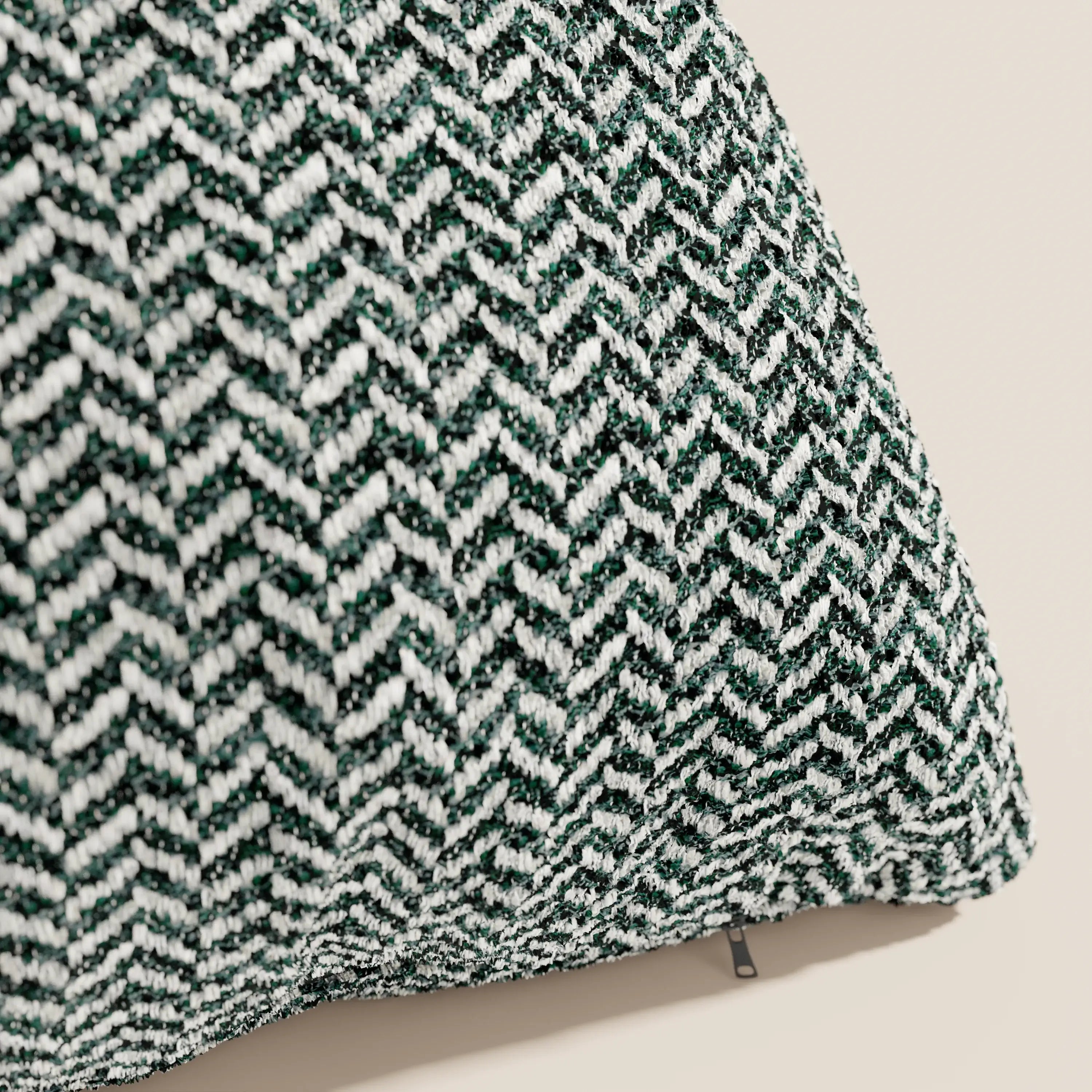 Primo piano del modello "Cuscino 45x45 in Lino" della linea Sorrento di Divani.Store, caratterizzato da un tessuto a motivo chevron verde e bianco, una cerniera discreta che ne facilita la rimozione e fodere lavabili in lavatrice, il tutto su uno sfondo beige neutro.