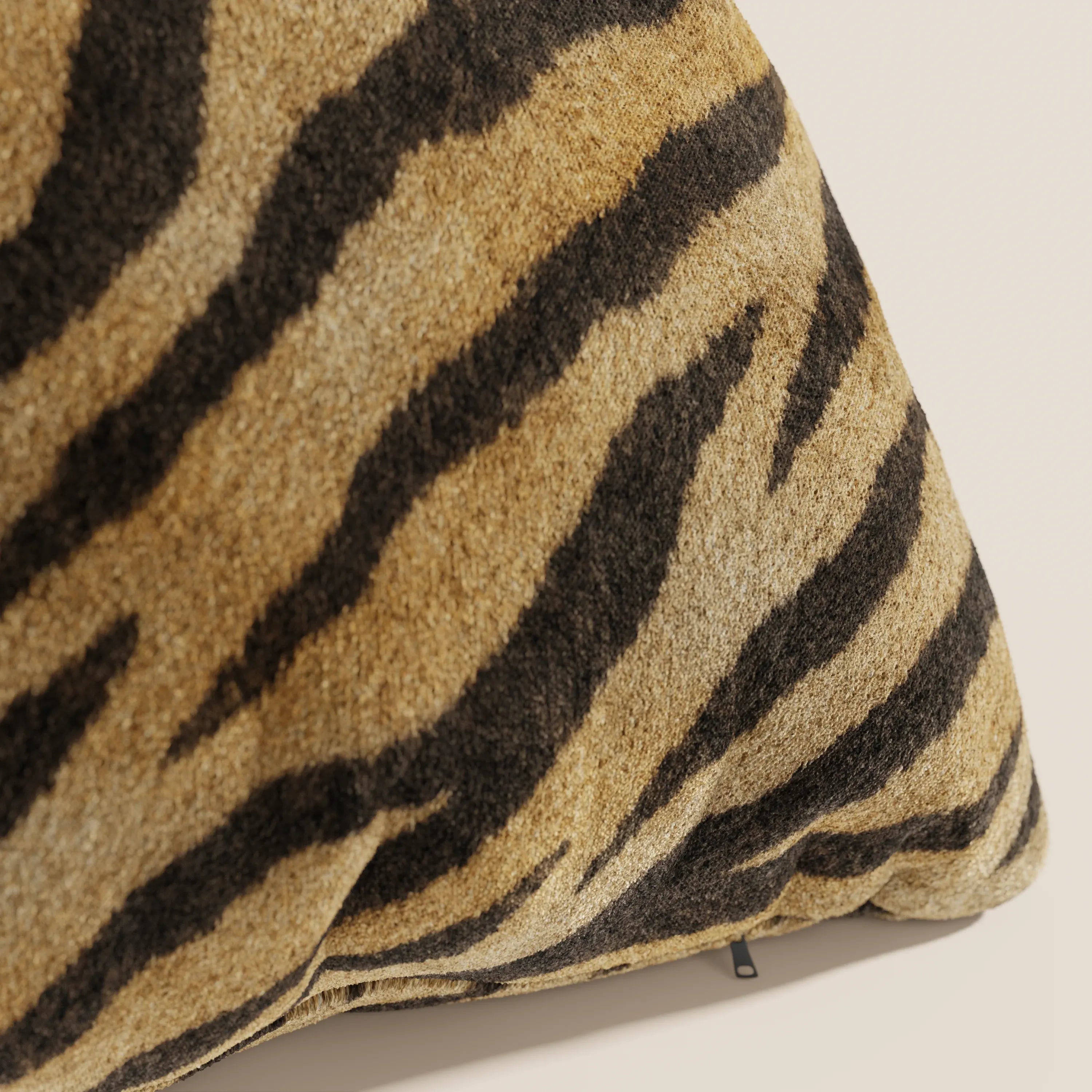 Primo piano del cuscino Wild della collezione Wild in microfibra impermeabile tigre di Divani.Store, caratterizzato da una forma triangolare in peluche e da strisce tigrate tan-nere che imitano la pelliccia della tigre, su uno sfondo chiaro.