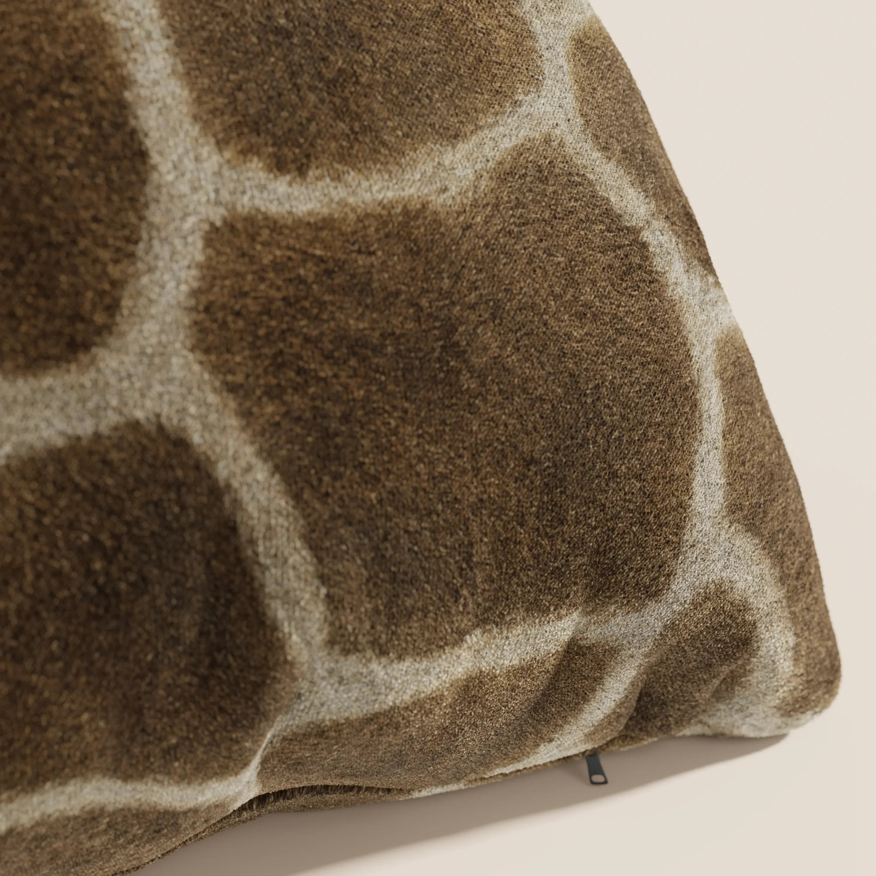 Un primo piano del cuscino Wild 45x45 della collezione Wild di Divani.Store mostra la microfibra impermeabile a motivo di giraffa, di colore marrone con macchie chiare, dalla consistenza vellutata e con una raffinata targhetta nera lungo il bordo.