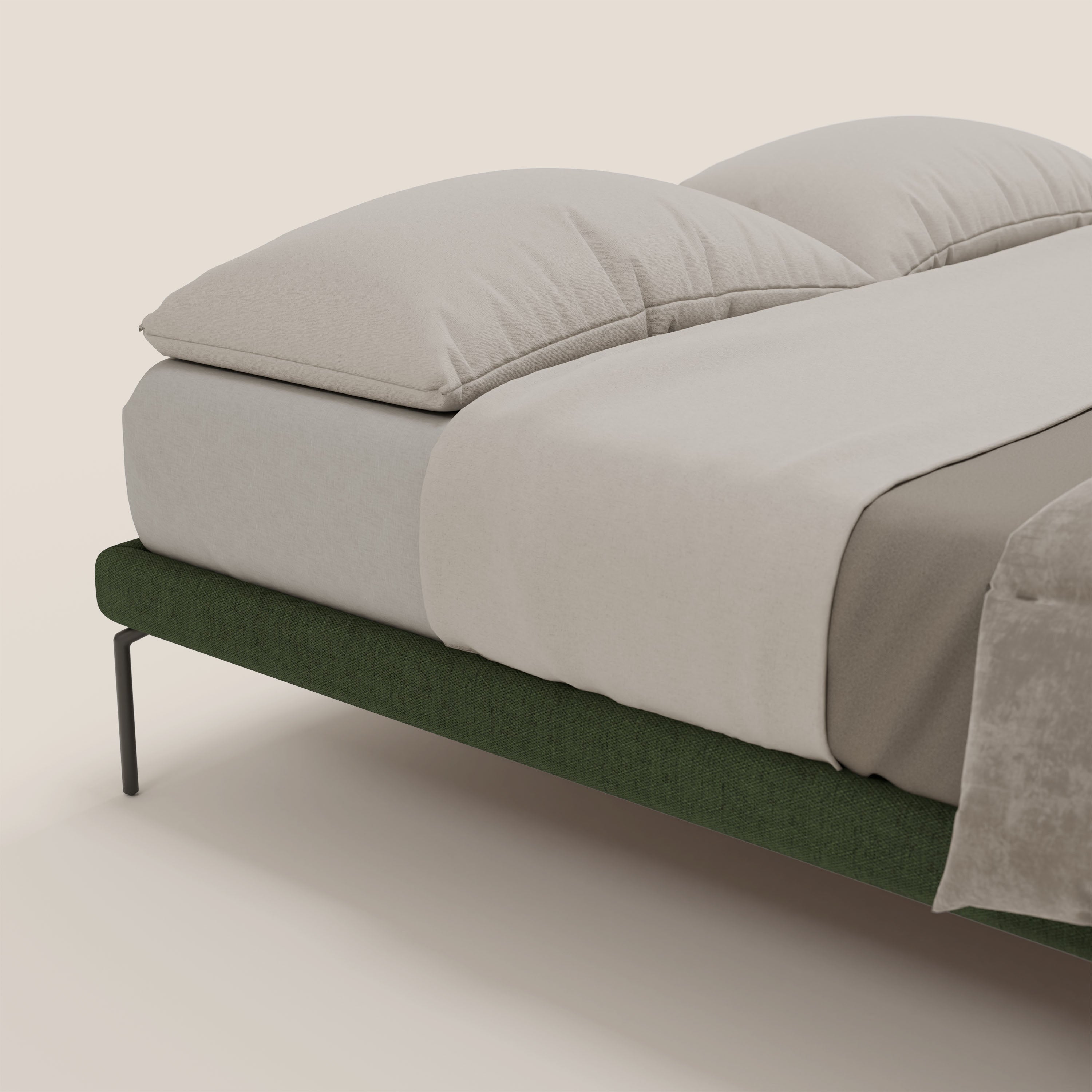Primo piano del sommier sfoderabile Letti.store Ring con gambe nere da 24 cm e tessuto impermeabile verde T14, abbinato a lenzuola beige chiaro, due grandi cuscini beige, una coperta tortora ai piedi, su uno sfondo beige chiaro.