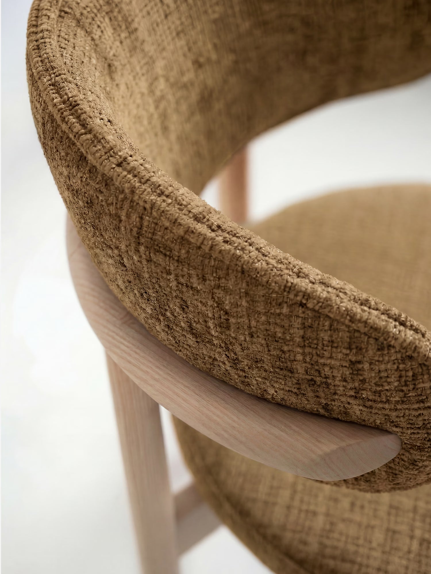 Primo piano della sedia imbottita Dafne di Divani.Store, caratterizzata da uno schienale curvo in ciniglia certificata OEKO-TEX® e da gambe in rovere massello naturale. L'immagine mette in risalto la raffinata lavorazione artigianale di questa elegante sedia in legno massello certificata. Sfondo leggermente sfocato.