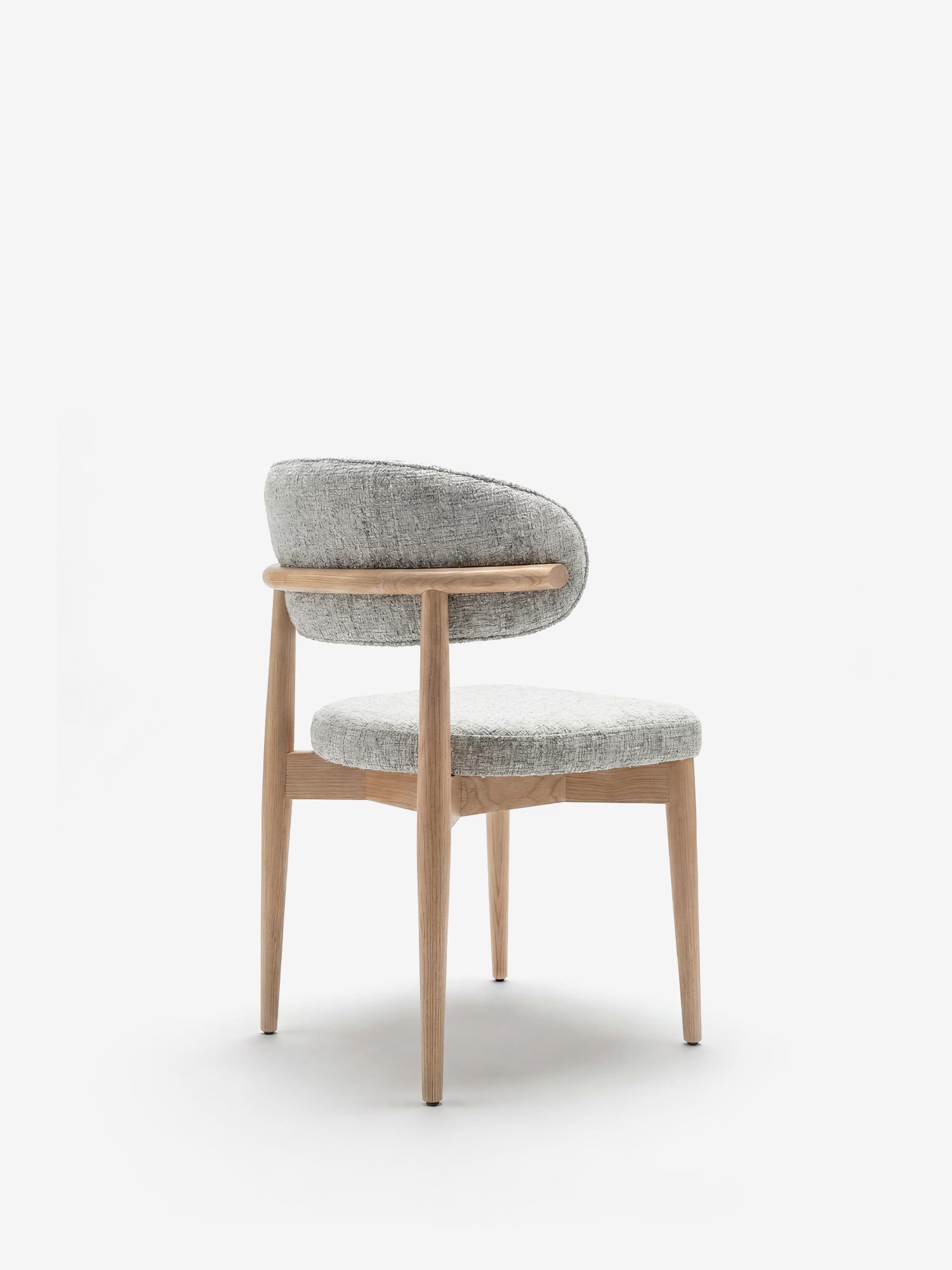 La sedia imbottita Dafne di Divani.Store presenta una struttura in rovere naturale massiccio e gambe in legno chiaro, con schienale curvo e seduta rotonda rivestite in tessuto ciniglia certificato OEKO-TEX®, qui raffigurata su uno sfondo bianco a tinta unita.