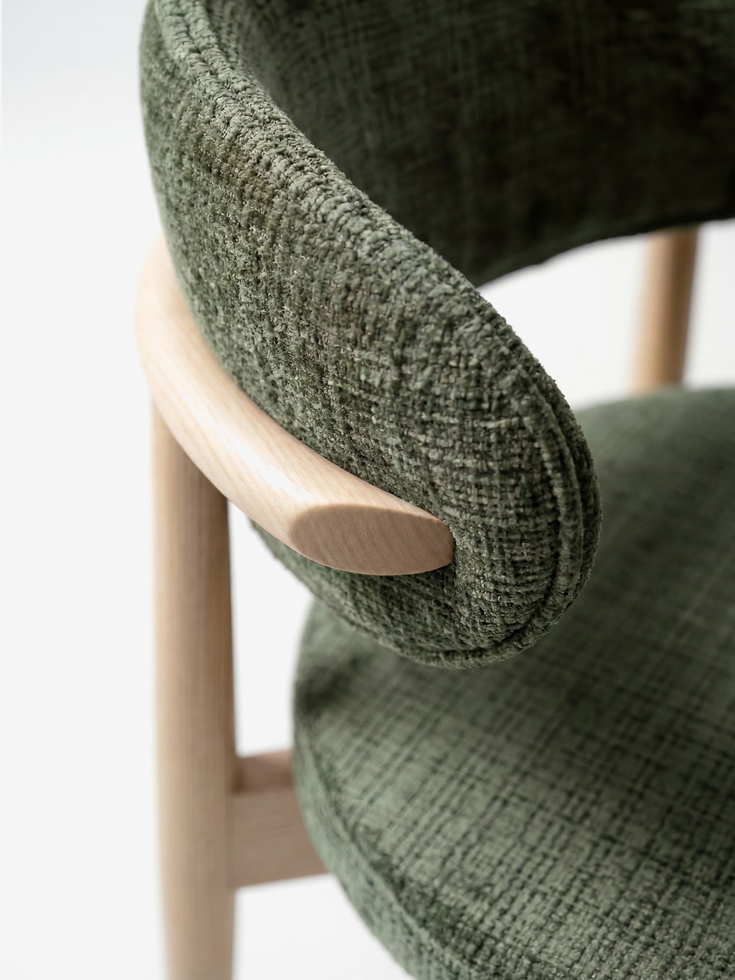 Primo piano della sedia imbottita Dafne di Divani.Store: schienale ricurvo in tessuto ciniglia verde certificato OEKO-TEX®, montato su una struttura liscia in rovere massello (rovere naturale), che mette in risalto il contrasto tra il morbido rivestimento e il legno chiaro.