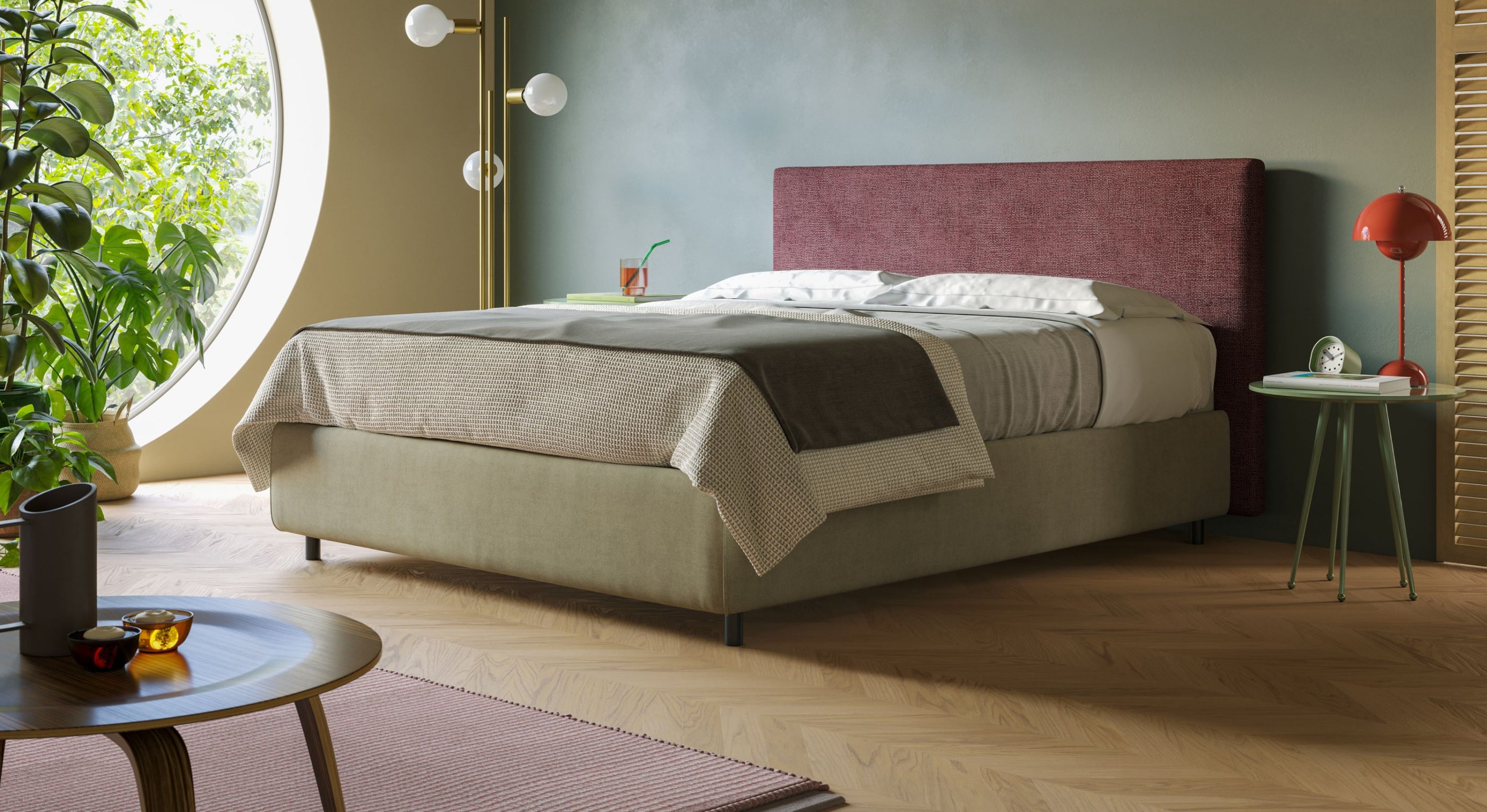 Camera da letto moderna con il sommier Sara con giroletto contenitore in tessuto impermeabile T02 panna di Letti.store, caratterizzato da una testata marrone, biancheria da letto neutra, tavolino verde con lampada rossa, piante vicino alla finestra rotonda, tavolino in legno e lampada da terra dorata.