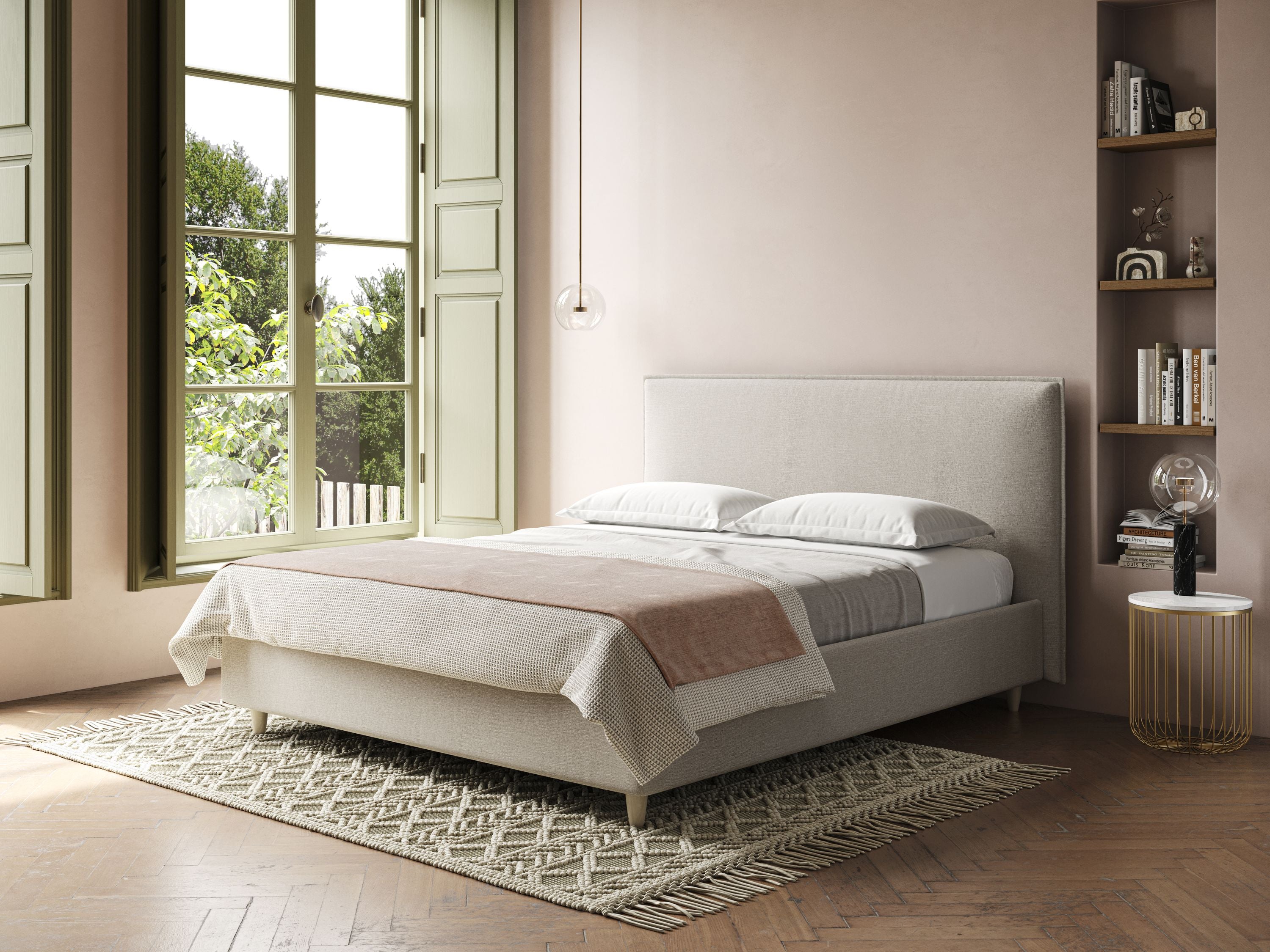 Una camera da letto illuminata dal sole con un'ampia finestra, persiane verde chiaro, un Costanza letto contenitore e sfoderabile in tessuto misto cotone impermeabile T13 panna di Letti.store con biancheria da letto bianca e copriletto marrone chiaro, tappeto a fantasia, tavolino rotondo, mensole a muro, pareti rosa e pavimento in legno.