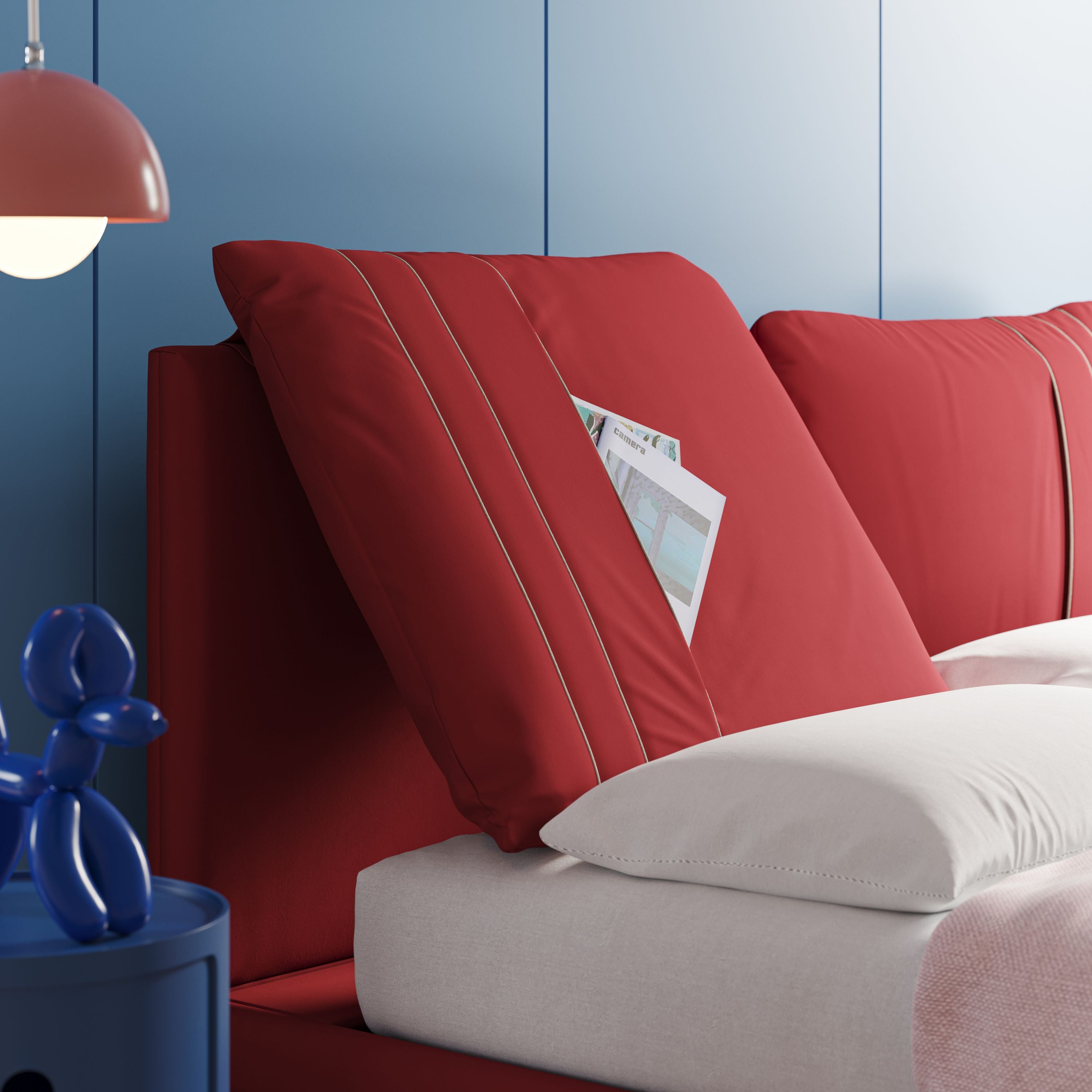 Il letto moderno Giselle di Letti.store, con cuscini della testata regolabili in microfibra T11 rossa con tasche, aggiunge fascino a questa camera azzurra. La biancheria da letto e la testiera bianche esaltano il design italiano, mentre il comodino blu espone una statuetta di cane a forma di palloncino.