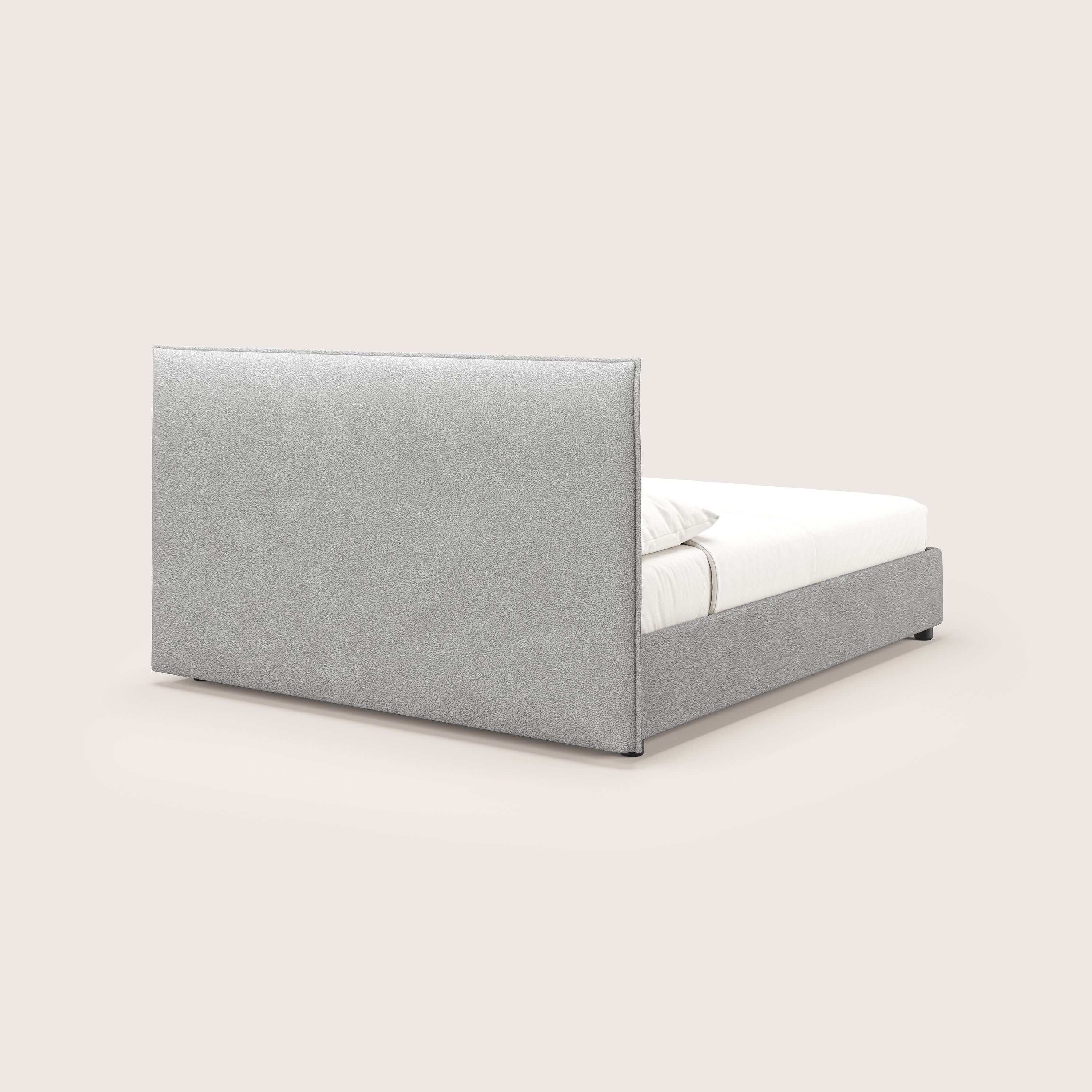 Il letto contenitore Nina di Letti.store è caratterizzato da un design minimale in microfibra grigia antimacchia, con testata rettangolare alta e struttura bassa. Viene presentato con materasso e cuscini bianchi, visto da dietro su uno sfondo beige.
