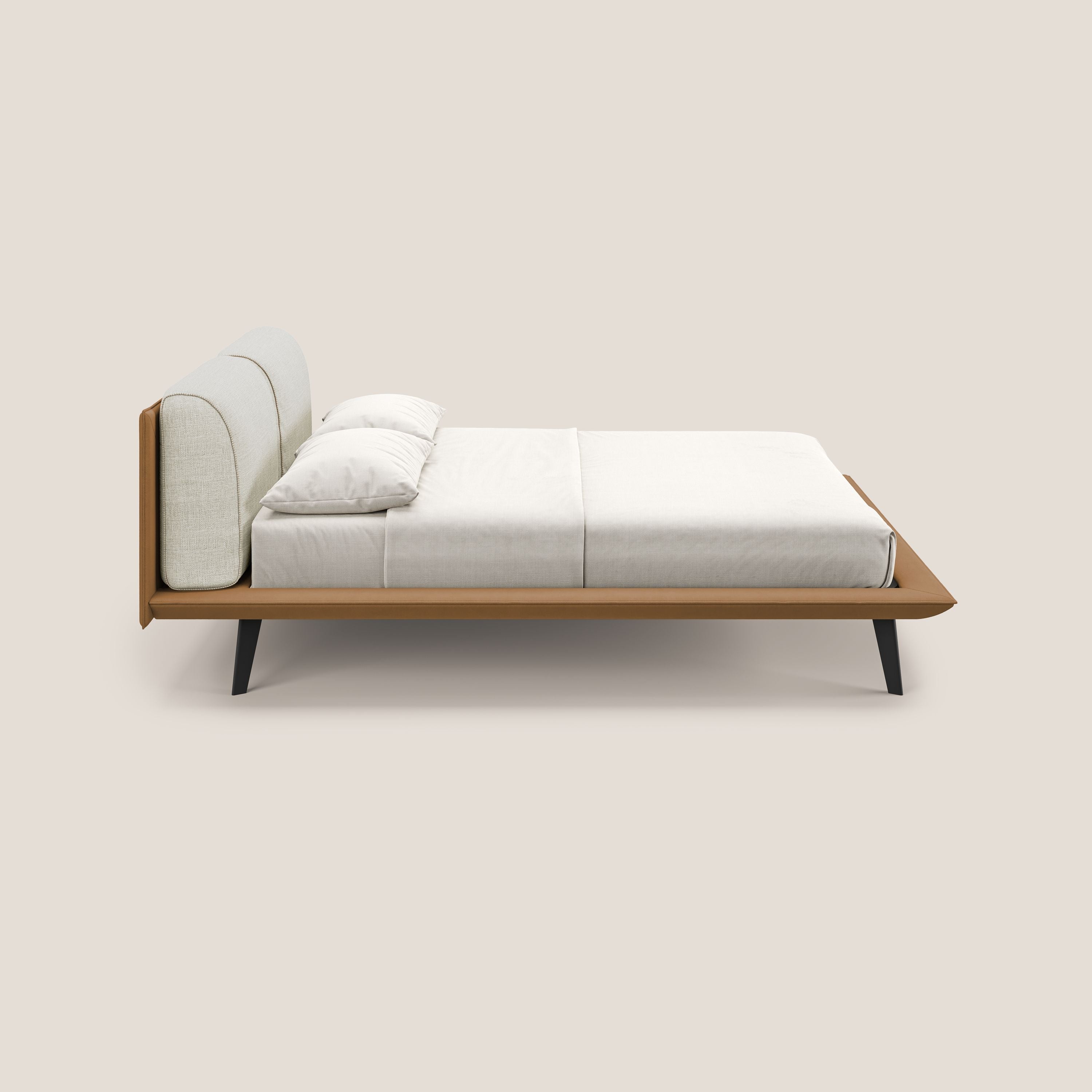 Il letto di design bicolore Petra di Letti.store è caratterizzato da cuscini in piuma, piedini in mogano e tessuto impermeabile T11 cuoio e T06 panna, ordinatamente realizzato con lenzuola e cuscini bianchi su sfondo beige tinta unita.