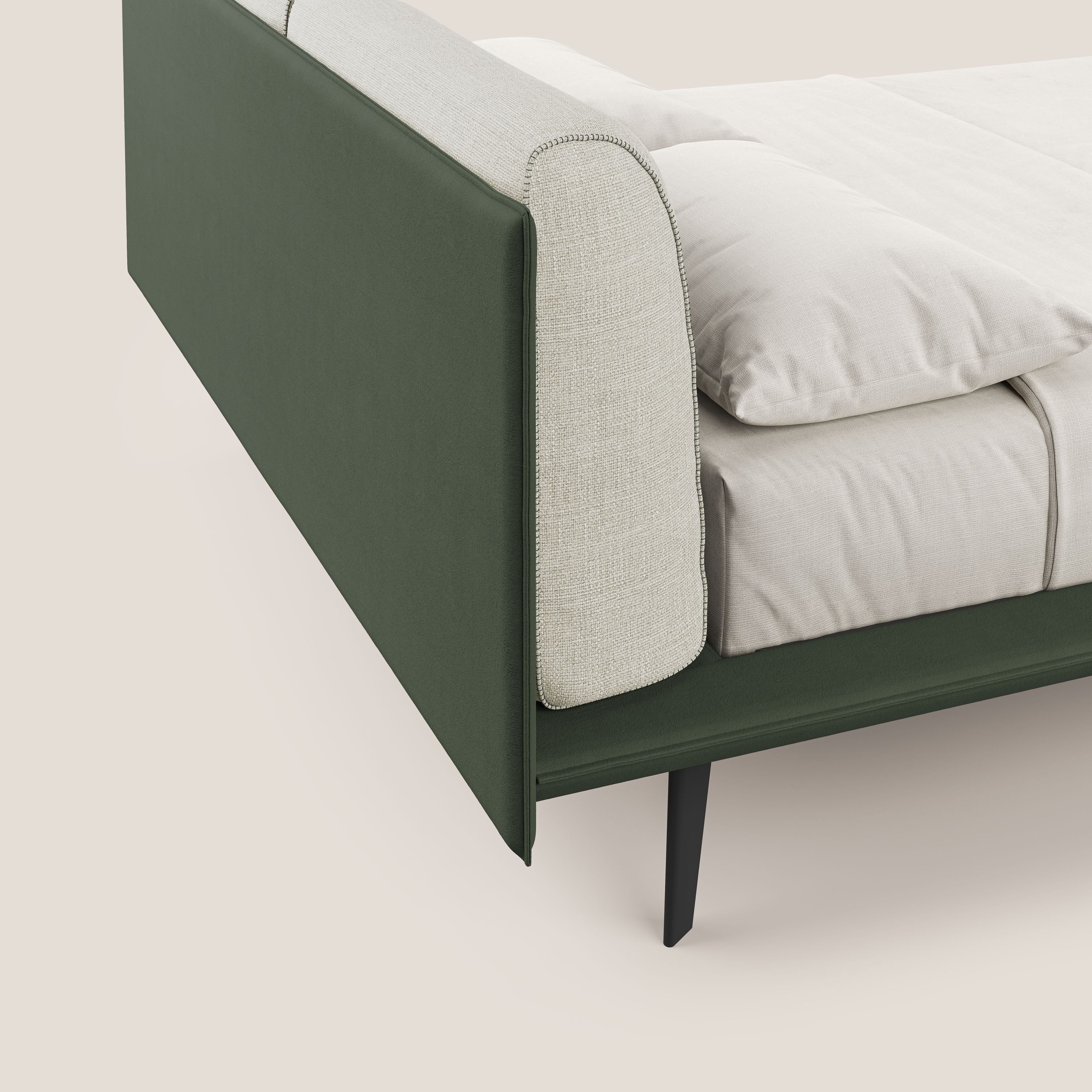 Il letto di design Petra di Letti.store è caratterizzato da un tessuto impermeabile bicolore verde-panna (T11/T06), da una testata imbottita in piuma e da sottili gambe angolari in mogano. Presentato in un'ambientazione luminosa da una visuale angolata.