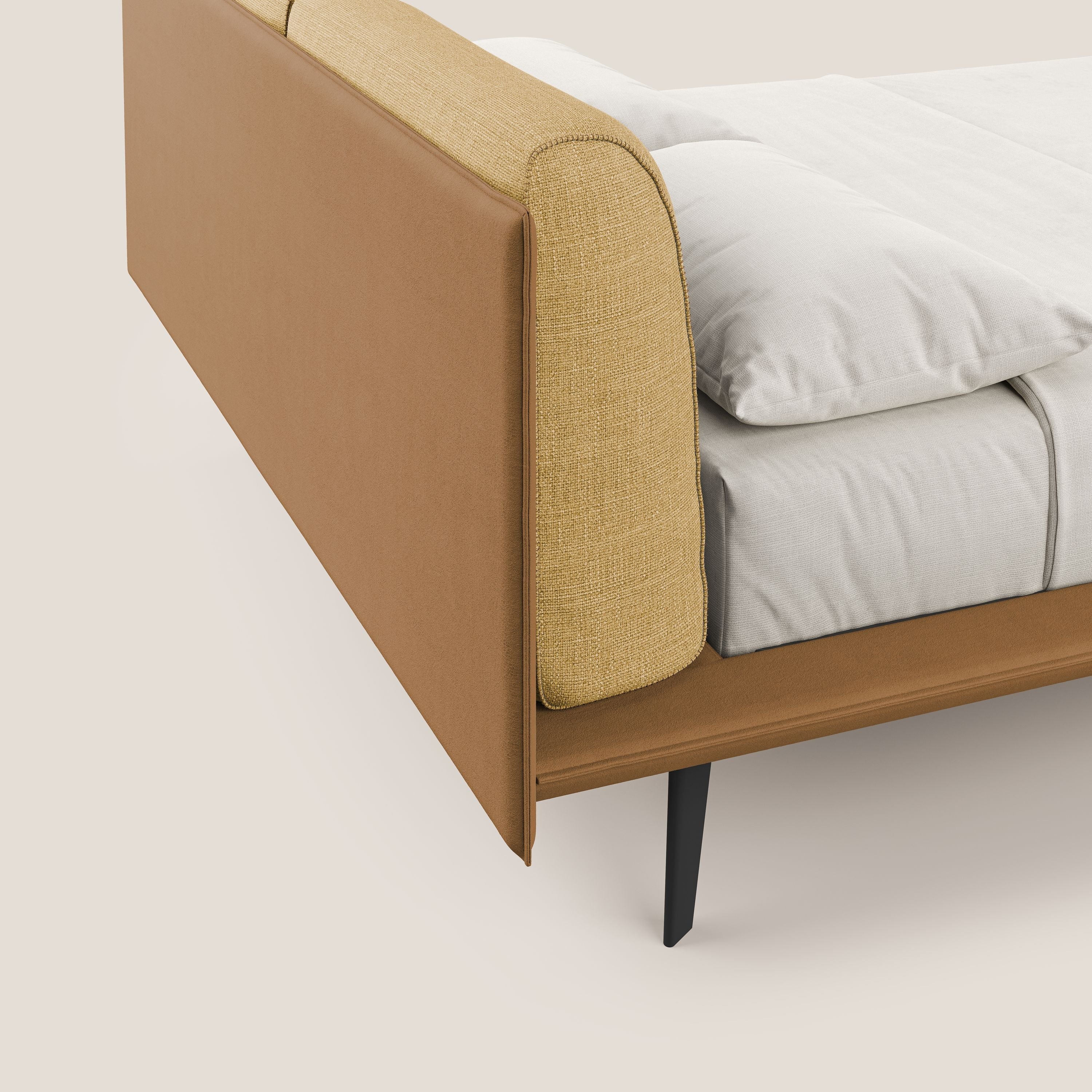 Un primo piano del letto di design Petra di Letti.store mostra il suo rivestimento bicolore impermeabile T11/T06 cuoio-giallo, i cuscini in piuma, la biancheria bianca e l'elegante piedino in mogano: linee moderne e stile sofisticato.