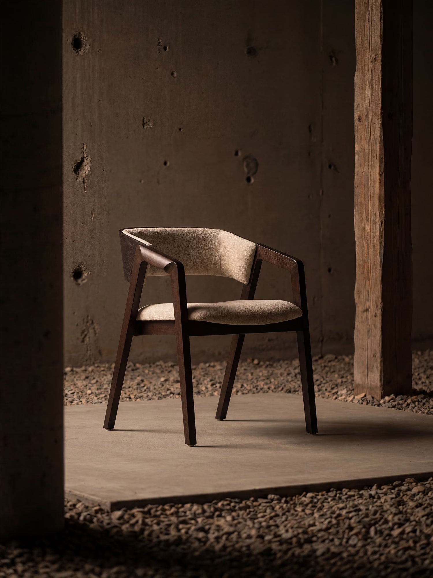 La sedia Etra di Divani.Store, realizzata in legno massello scuro con braccioli e rivestita in ciniglia beige, si distingue per il suo design moderno ed elegante in uno spazio industriale con travi a vista e pareti in cemento.