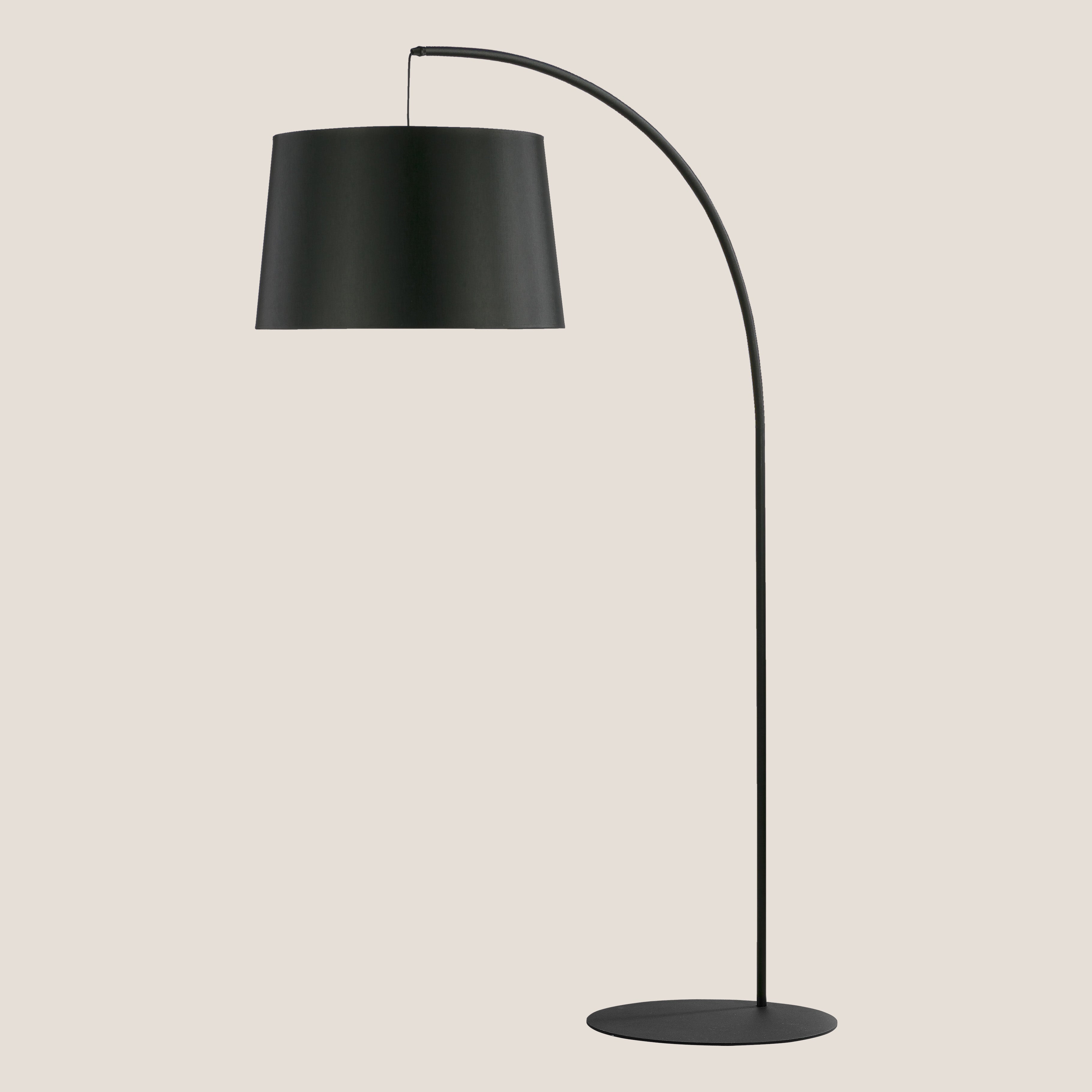 La lampada da terra con paralume in tessuto Fabian di Divani.Store è caratterizzata da un design moderno di colore nero con base rotonda, supporto sottile e curvo e ampio paralume in tessuto, che crea un look minimalista su uno sfondo beige chiaro.