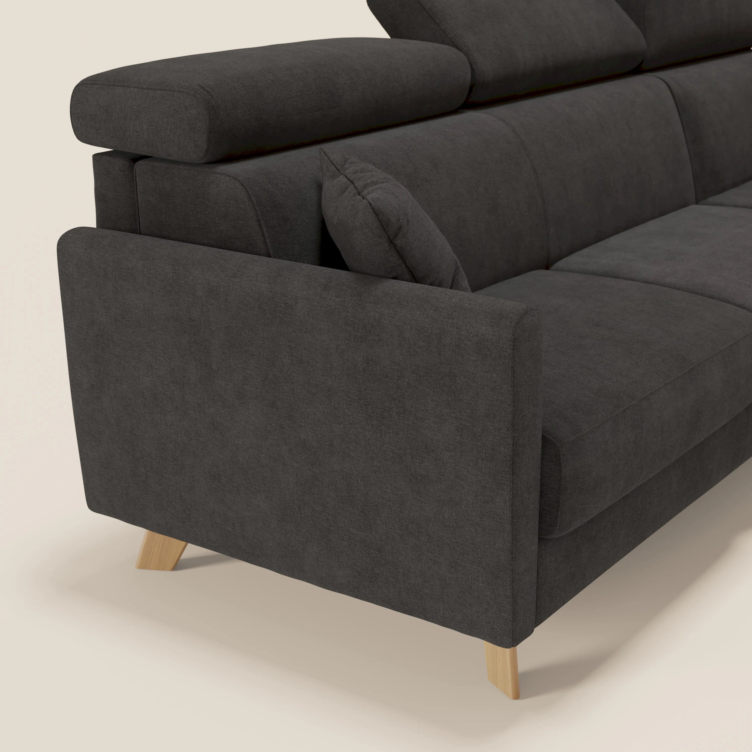 Vista laterale ravvicinata del divano letto angolare sfoderabile Francy di Divani.Store in tessuto smacchiabile T17 antracite con penisola contenitore, poggiatesta reclinabile, bracciolo spesso e cuscino, su sfondo bianco sporco.