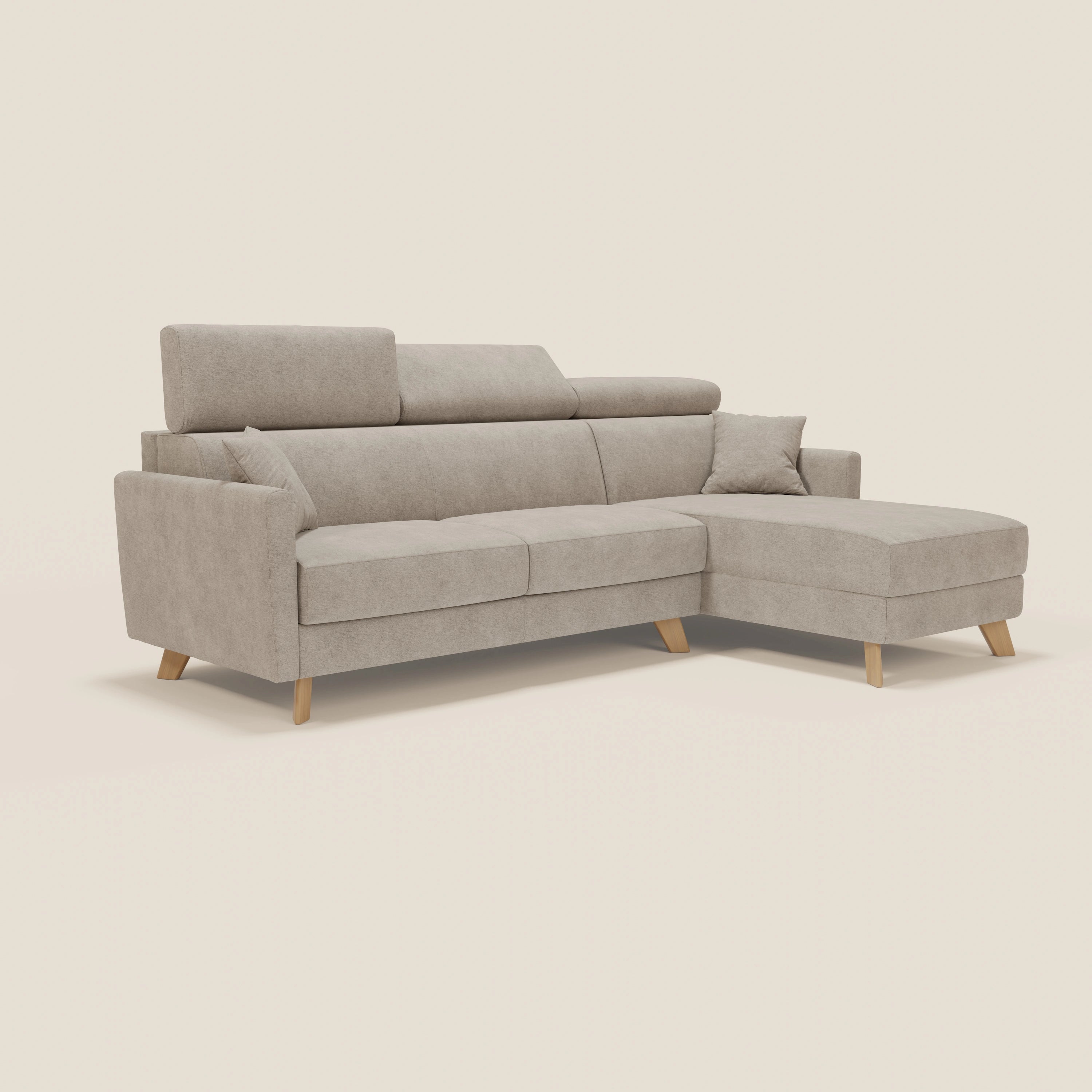 Divano a L Francy beige di Divani.Store, con tessuto T17 antimacchia, chaise longue a destra, poggiatesta regolabili, gambe in legno angolate, tre cuscini e un cuscino coordinato, su uno sfondo bianco sporco.