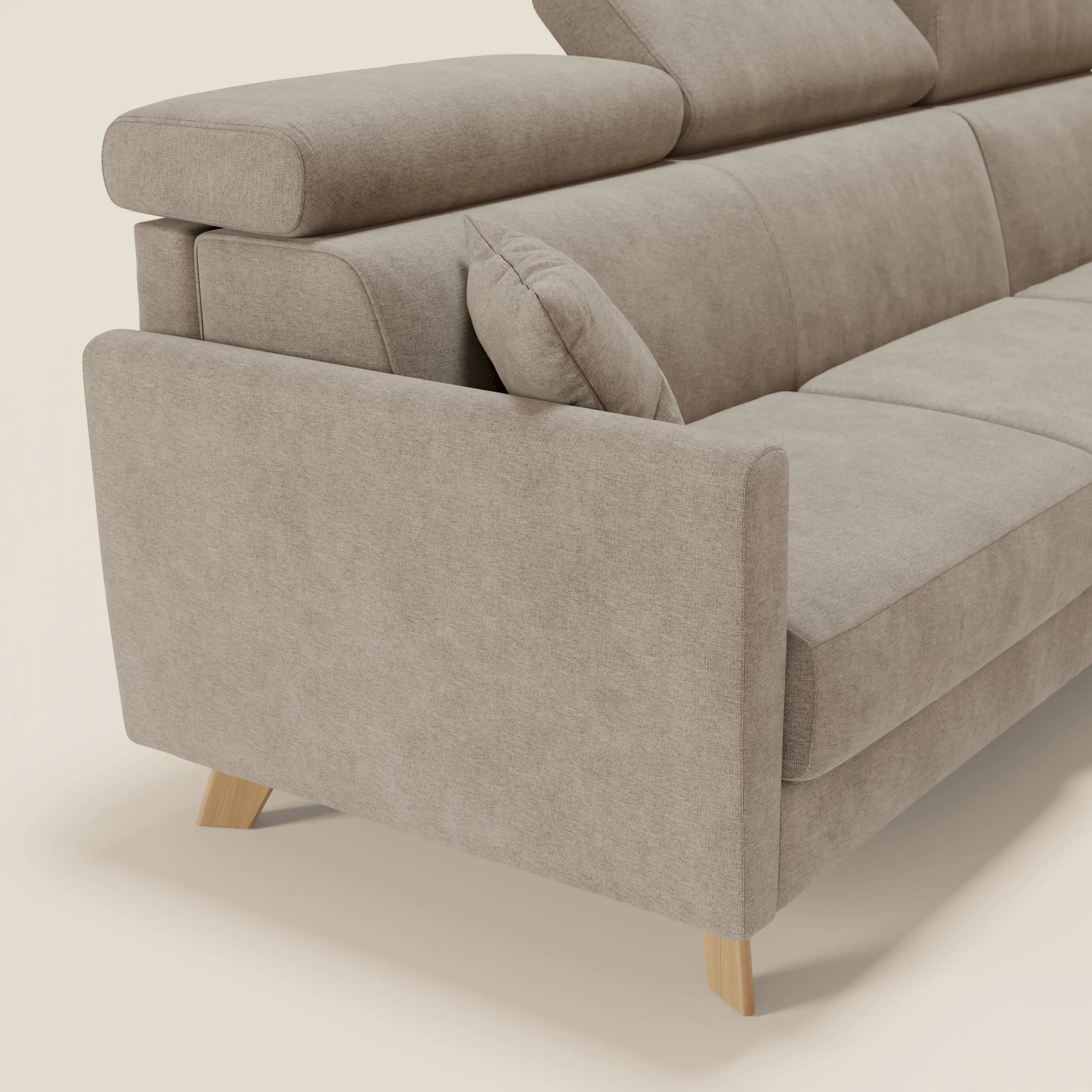 Primo piano del divano letto angolare sfoderabile Francy di Divani.Store in T17 beige, con gambe in legno, poggiatesta reclinabili, poltrona contenitore e design nordico e minimalista. Il cuscino singolo si appoggia al bracciolo su uno sfondo chiaro.